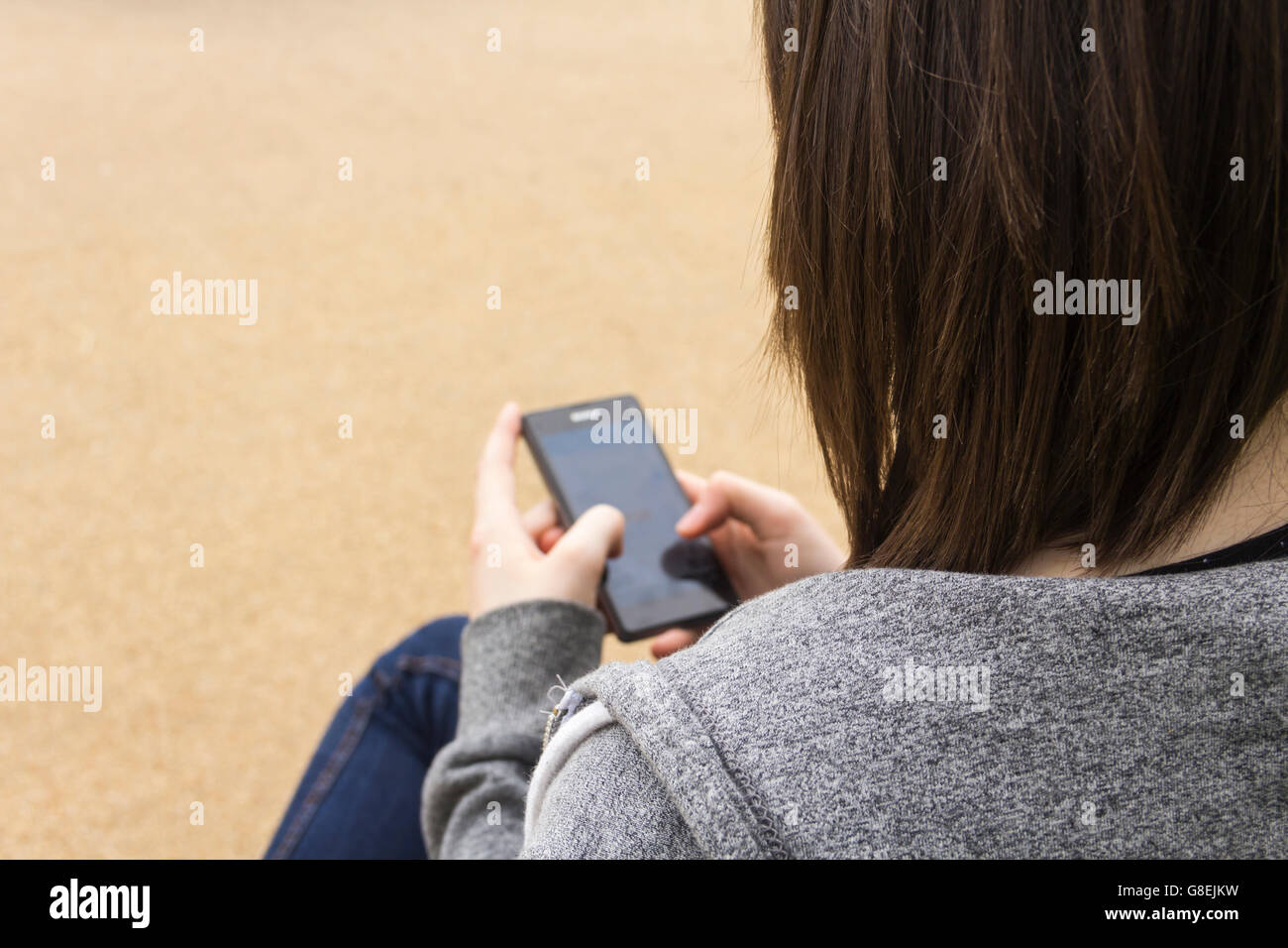 Junge Frau, Erwachsene oder späten Teens, sitzt auf einer Parkbank, SMS oder sonst mit ihrem Smartphone. Stockfoto