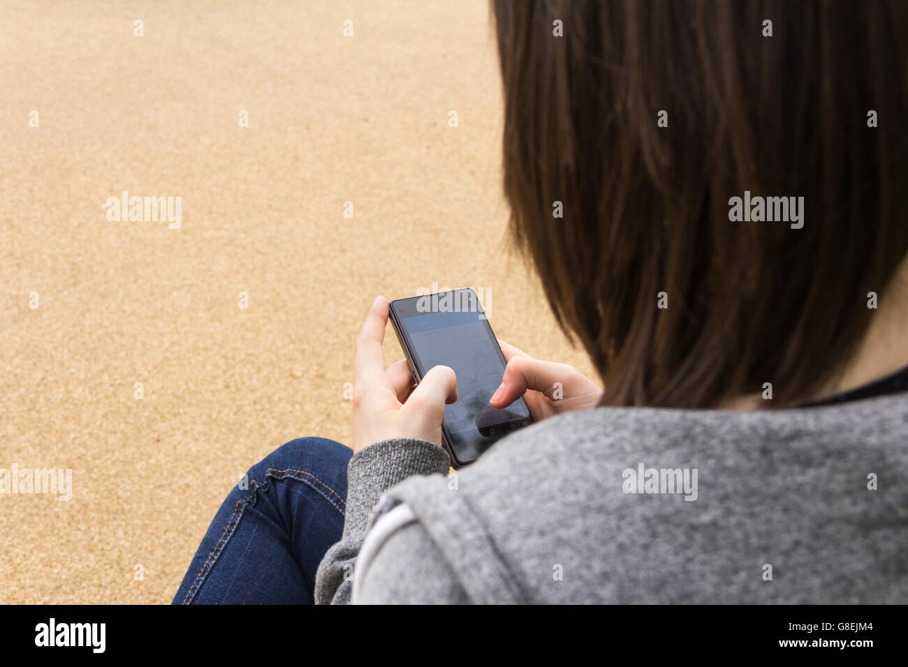 Junge Erwachsene oder späten Teens Frau sitzend, über die Schulter, SMS oder sonst mit ihrem Smartphone gesehen. Fokus liegt auf Telefon. Stockfoto
