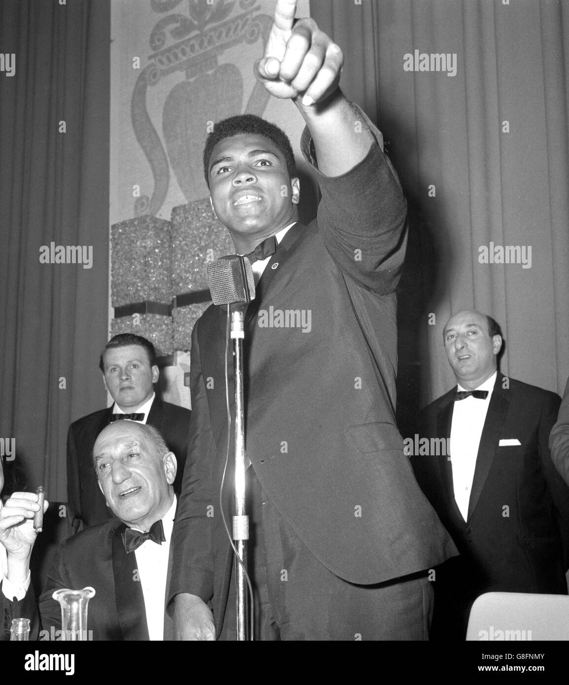 Muhammad Ali zeigt auf den anderen Raum und ruft Henry Cooper im London Hilton Hotel in Park Lane an, wo der Weltmeister bei einem Boxenabendessen im Anglo-American Sporting Club zu Gast war. 'Wenn er hier wäre, würde ich ihn jetzt bekämpfen', erklärte Ali. Cooper wird ihn am 21. Mai im Arsenal Stadium um den Weltmeistertitel herausfordern. Stockfoto
