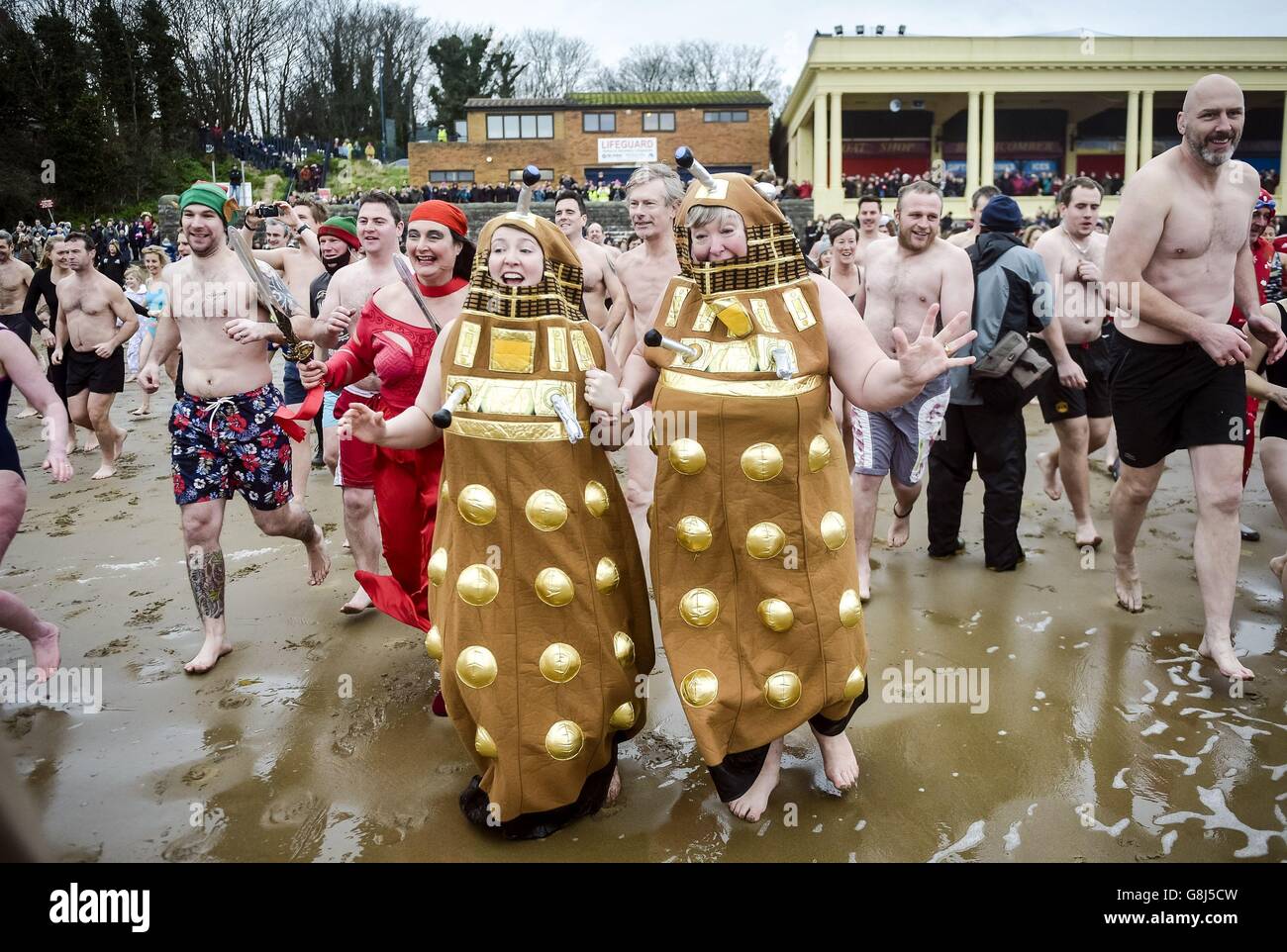 Auf Barry Island, in der Nähe von Cardiff in Wales, rasten Menschen in schicken Kleidern ins Meer, wo das jährliche Schwimmen am Neujahrstag stattfindet. Stockfoto