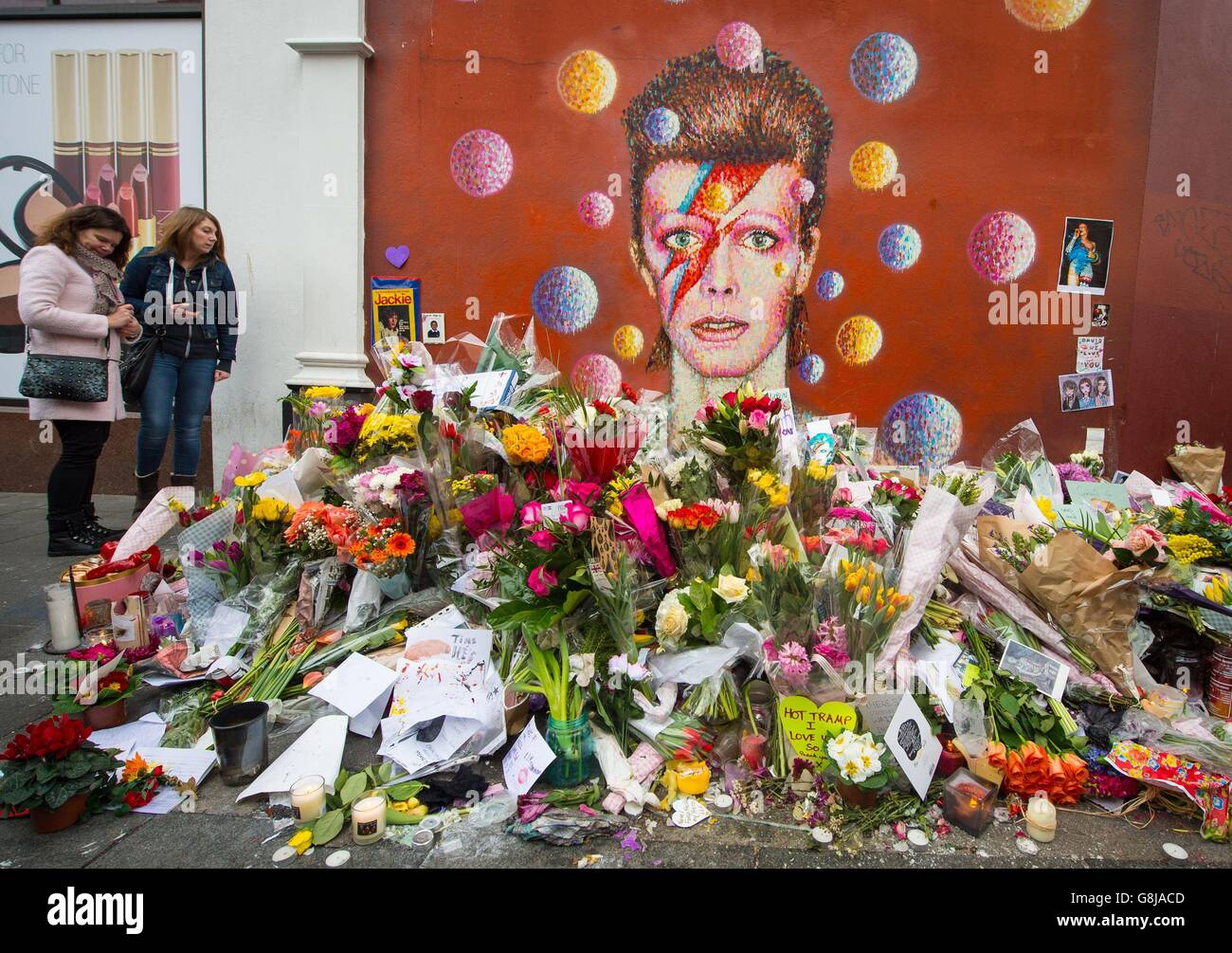 Die Menschen sehen Blumen, die an einem Wandgemälde des Musikers David Bowie in Brixton, im Süden Londons, nach der Ankündigung dieses Todes gestern zurückgelassen wurden. Stockfoto