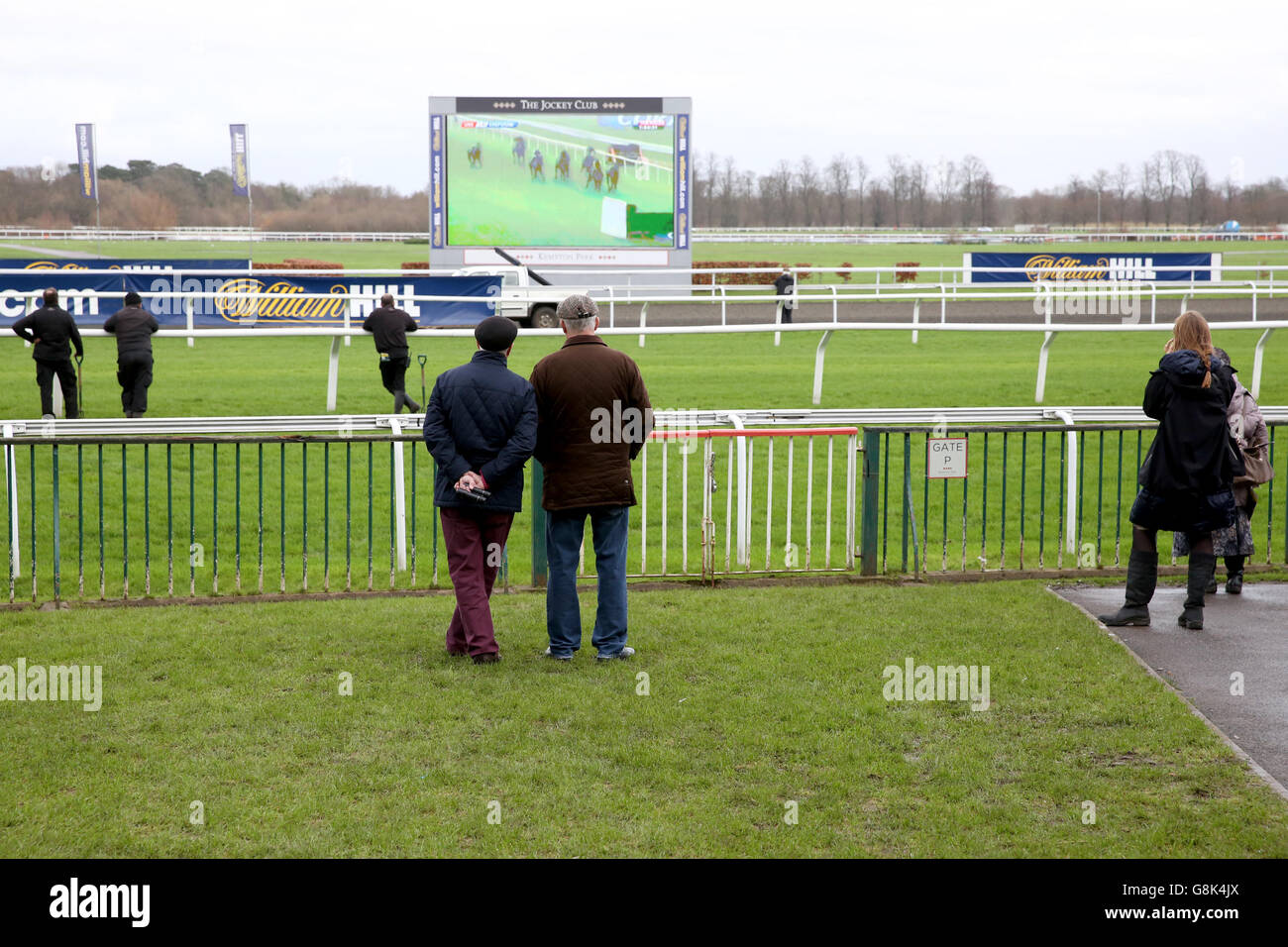 Racegoers sehen sich eine Wiederholung der Aktion auf dem Riesen an Bildschirm bei den Kempton Park Races Stockfoto