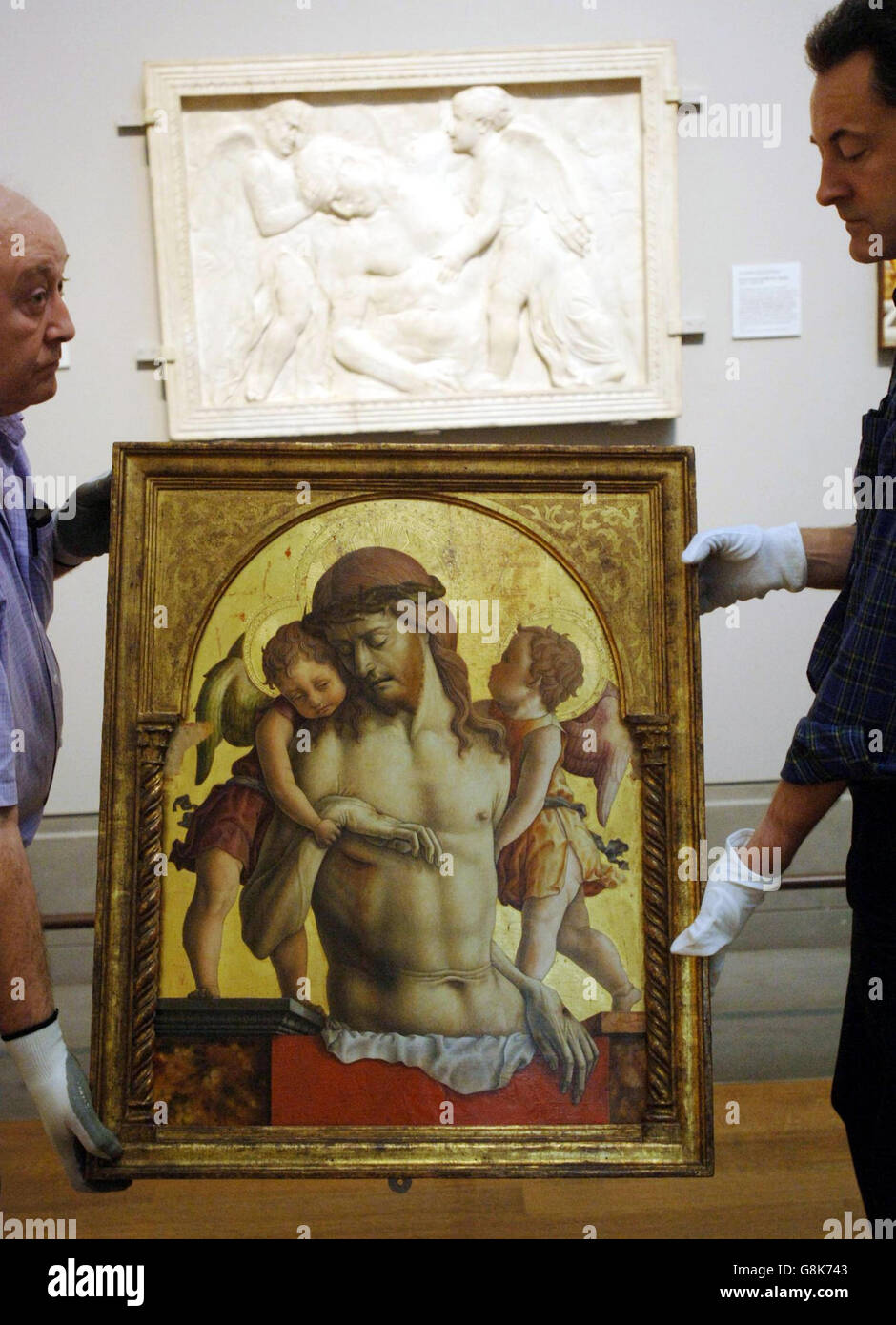 Crivellis 'Dead Christ supported by Two Angels' wird in Position gebracht, neben Donatellos Marmorrelief 'Dead Christ tended by Angels', das das Gemälde inspirierte. Stockfoto