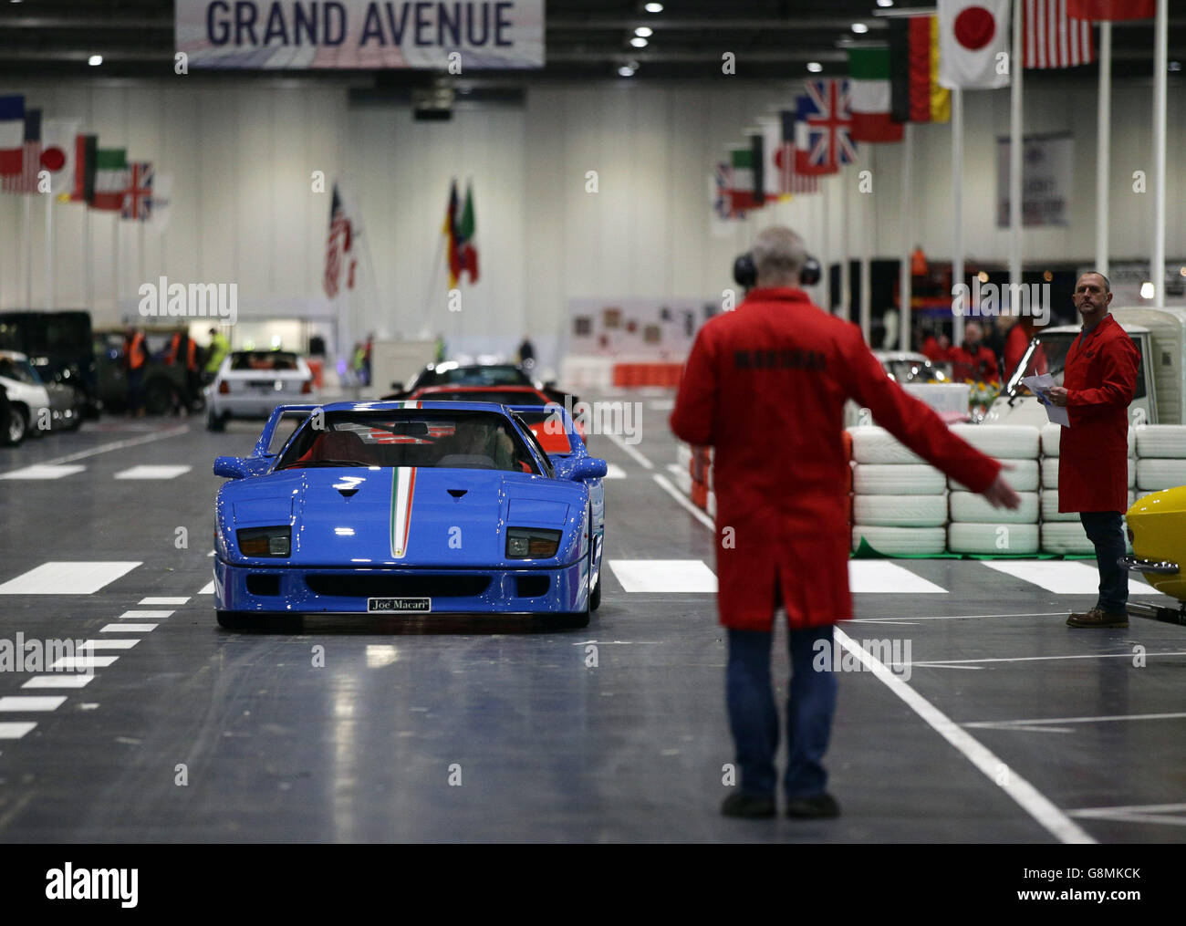 Ein Ferrari wird von einem marshall auf der Grand Avenue, auf der London Classic Car Show, in Excel im Osten Londons, geleitet. Stockfoto