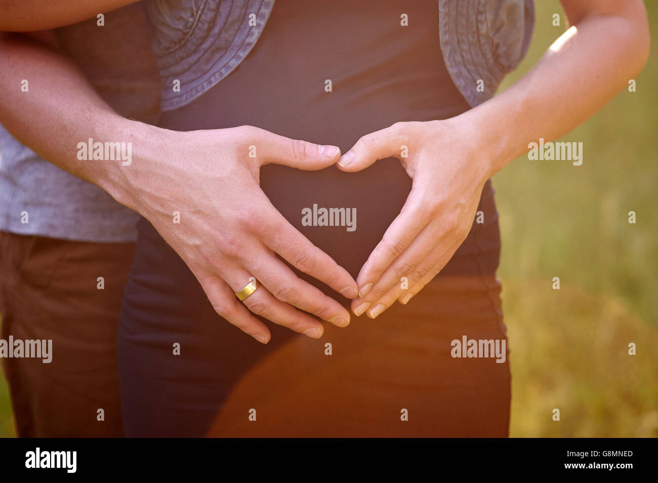 Schwangeren Bauch mit Finger-Herz-Symbol. Schöne junge schwangere Frau und ihr Mann zusammen ihren schwangeren Bauch streicheln Stockfoto