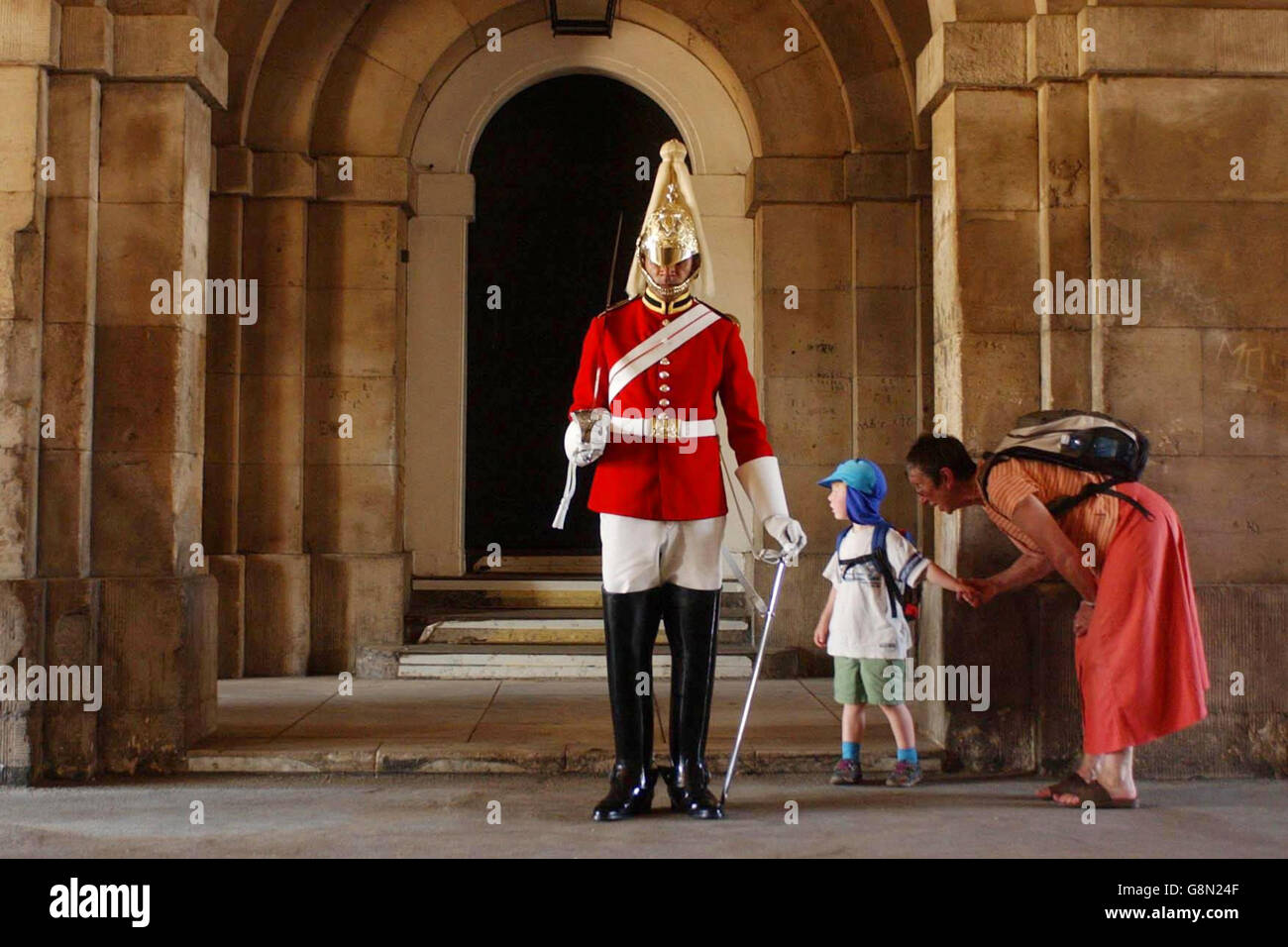 Eine Besucherin ermutigt ihren Sohn, einen Wächter, der bei der Horse Guards Parade im Zentrum von London aus der Sonne steht, mit einem zaghaften Blick zu betrachten. Stockfoto