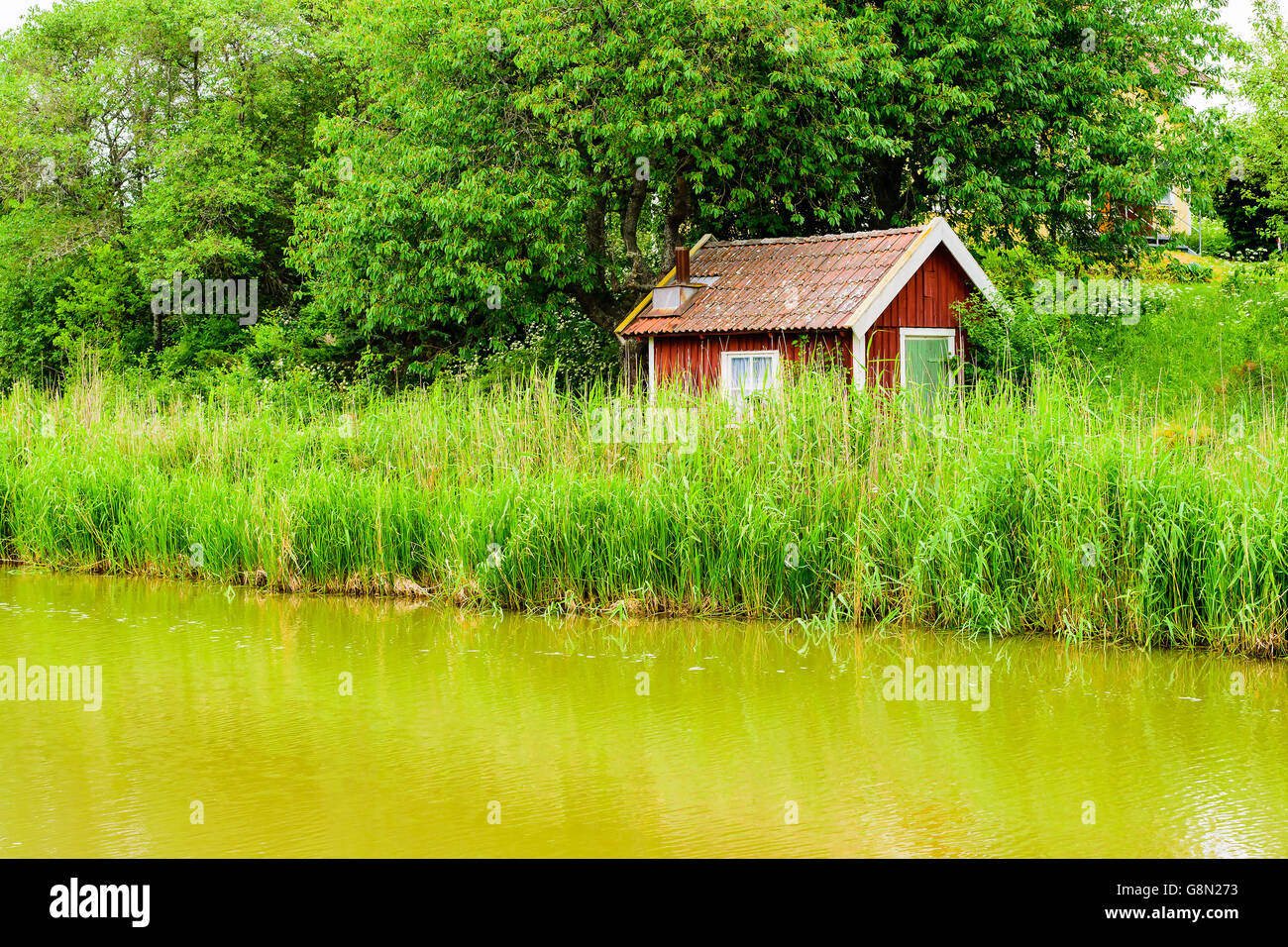 Sehr kleines und altes Holzhaus in der Nähe von einem Kanal oder Fluss. Reed fast Decken des Gebäudes. Ein kleinen Schornstein ist sichtbar im r Stockfoto