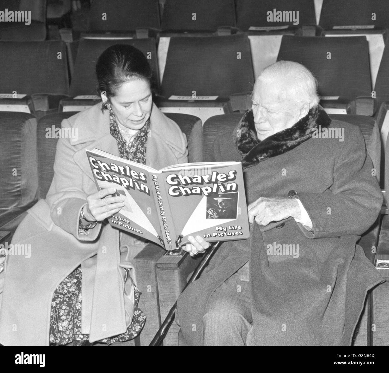 Charlie Chaplin, 85, und seine Frau Oona schauen sich sein Buch My Life in Picturs im Kino des Starlight Room im Mayfair Hotel an. Chaplins Buch, herausgegeben von Bodley Head, geht morgen in den Handel. Stockfoto