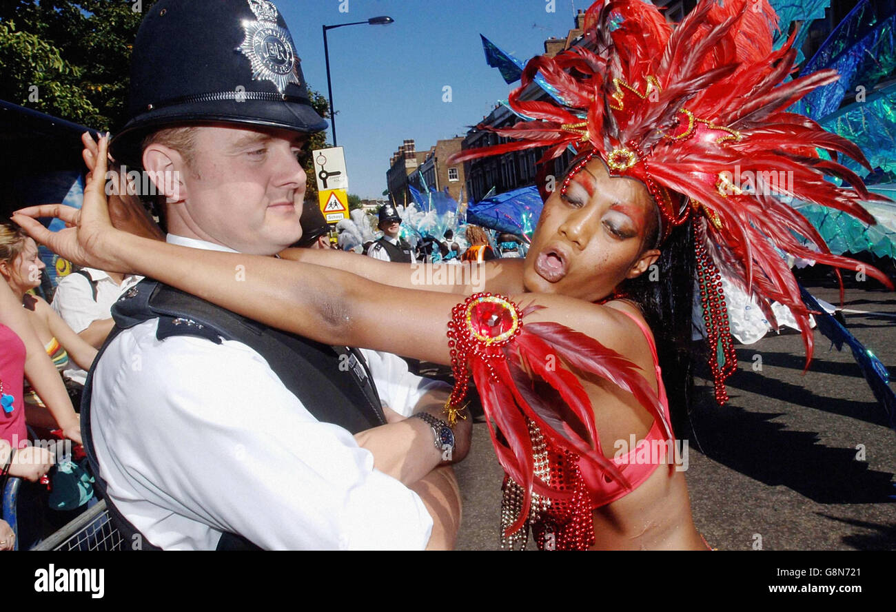 Ein Nachtschwärmer aus Trinidad tanzt mit einem widerwilligen Polizisten beim Notting Hill Carnival im Westen Londons. Die Straßen von Notting Hill sind vollgepackt, während Tausende am letzten und geschäftigsten Tag des Karnevals in strahlendem Sonnenschein tanzten. Stockfoto