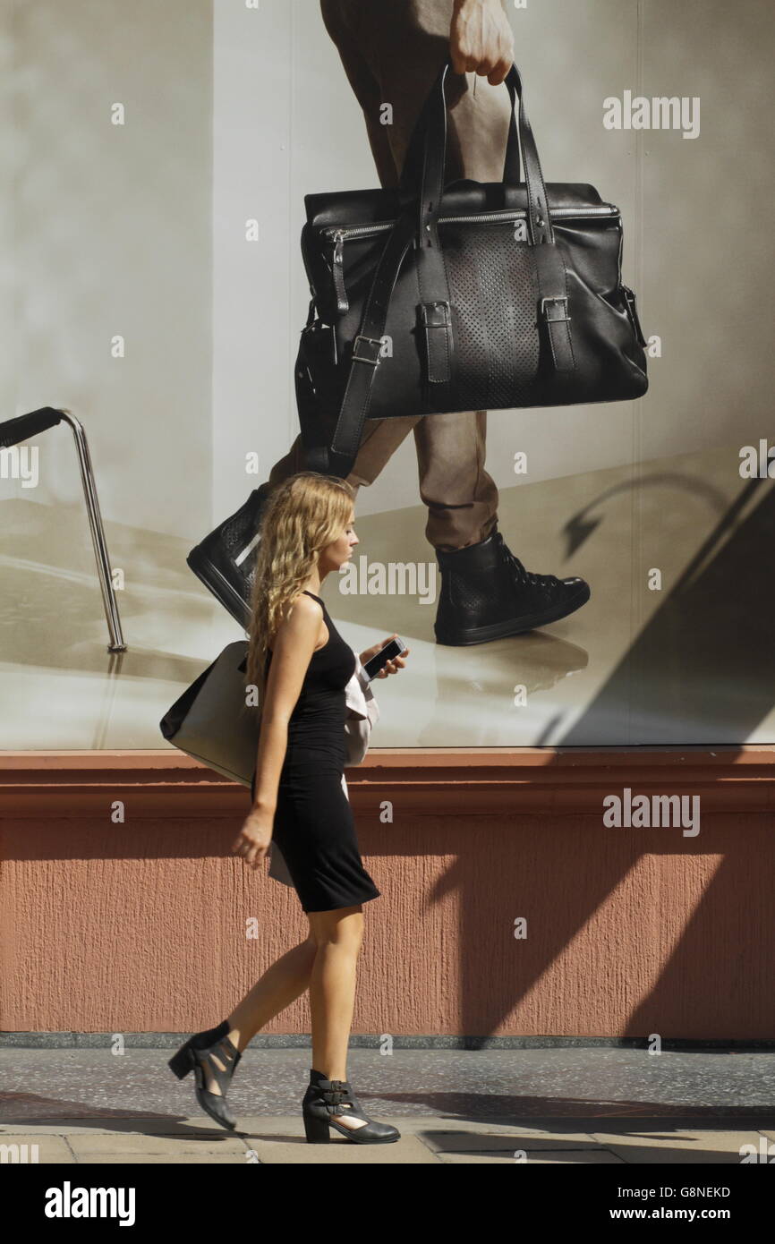 Modische Frau in schwarz repliziert die Schritte des Plakats hinter ihr New Bond Street, London. Stockfoto