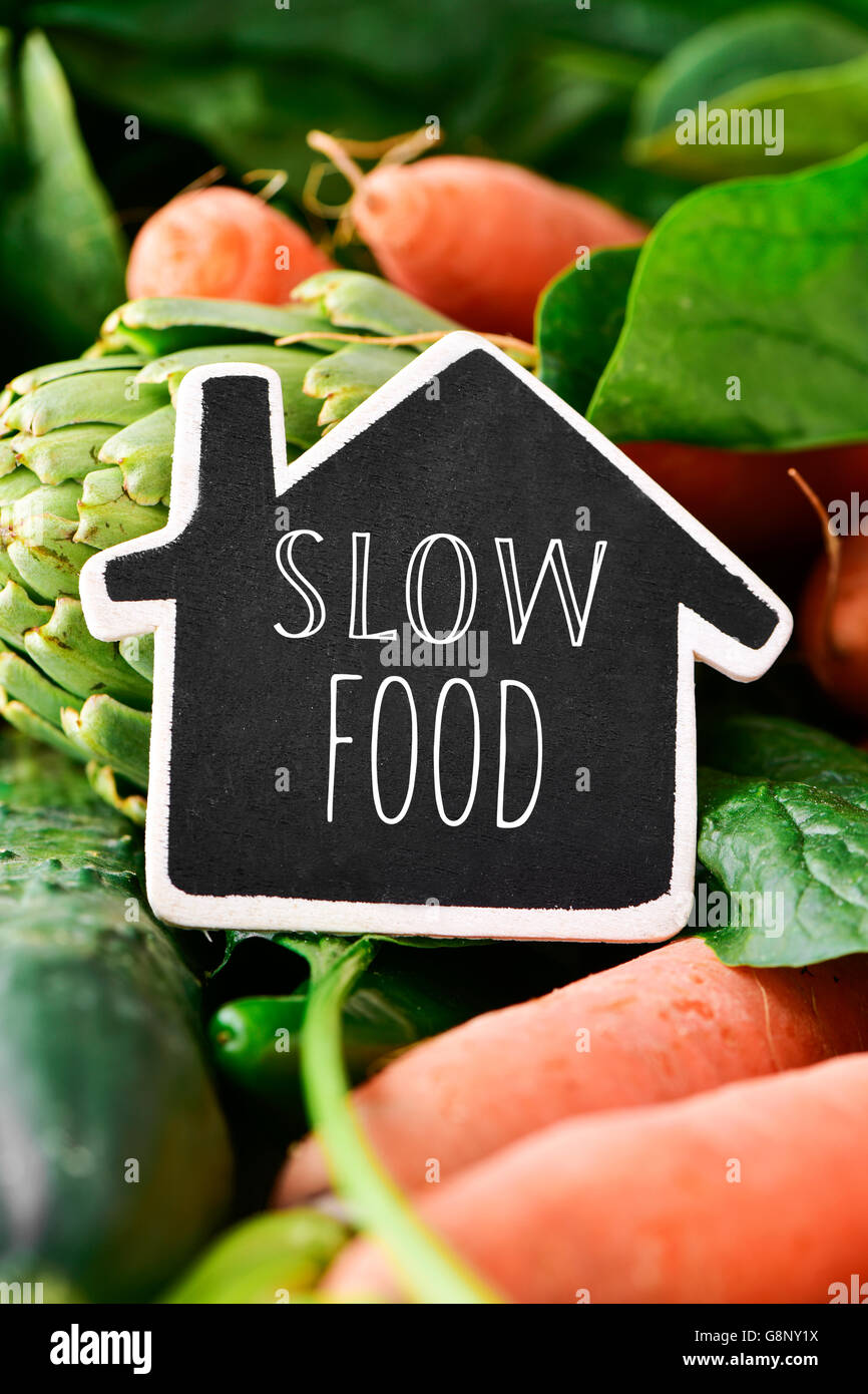Nahaufnahme von einer Haus-förmigen Tafel mit dem Text slow Food platziert auf einem Stapel von einigen verschiedenen rohes Gemüse wie Gurken Stockfoto