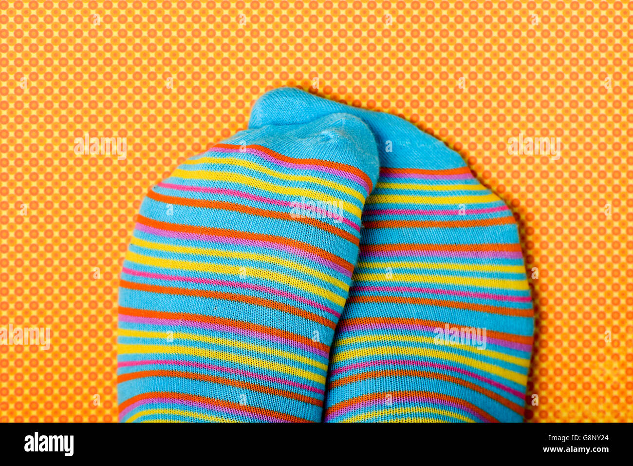 Nahaufnahme einer Person seine oder ihre Füße tragen buntere gestreift gemusterte Socken, auf eine orange und gelb gemusterten Zeitmessung reiben Stockfoto
