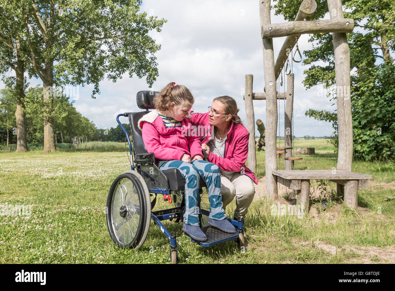 Eine behinderte Person in einem Rollstuhl entspannende außerhalb mit Hilfe von Freiwilligen Pflegedienst Stockfoto