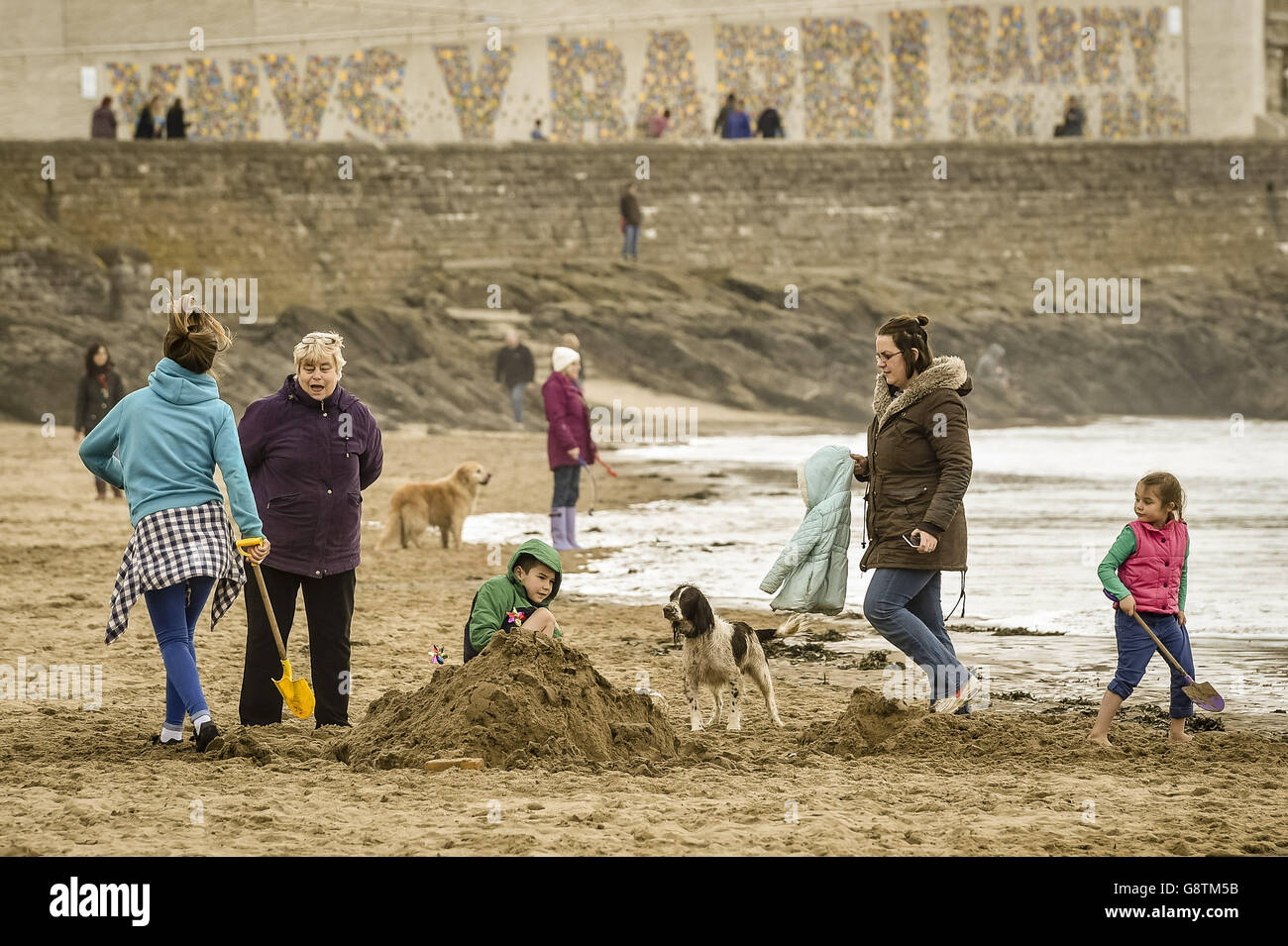 Die Leute spielen am Strand von Barry Island, Wales, wo das Wetter bedeckt und trüb ist. Stockfoto