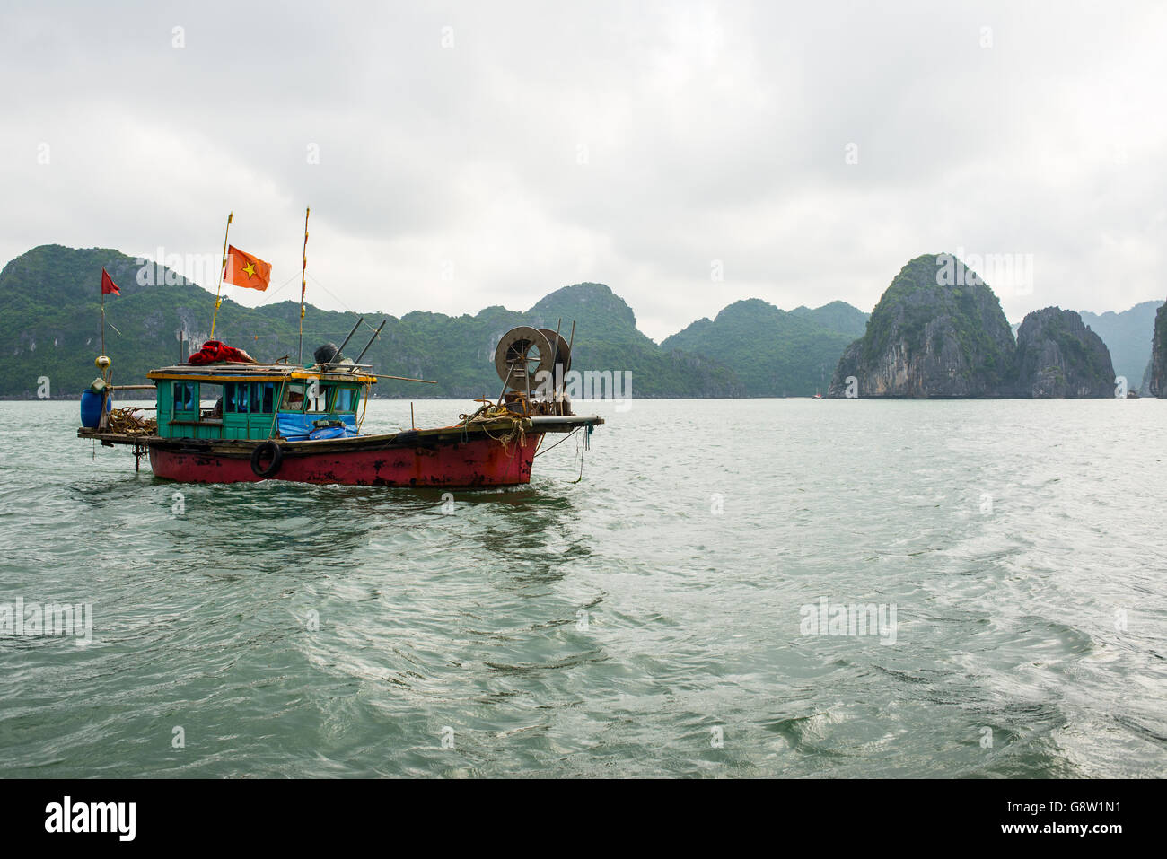 Altes Fischerboot mit Vietnam Flagge segeln in den ruhigen Gewässern um die Insel Cat Ba, Vietnam. Stockfoto