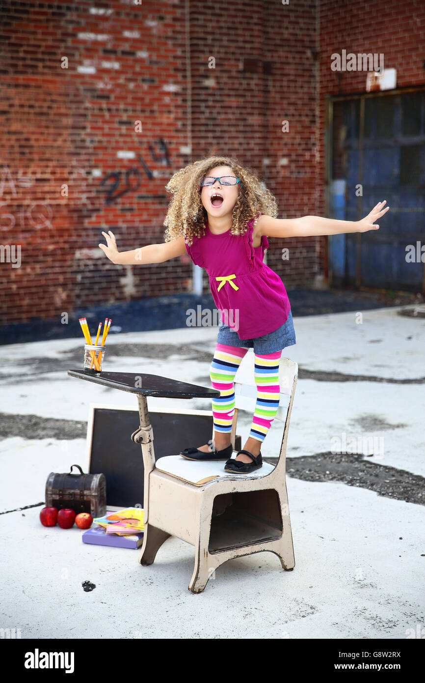 kleines Mädchen steht auf ihrem Stuhl während lächelnd in ein outdoor, städtischen Einstellung-zurück zur Schule Stockfoto
