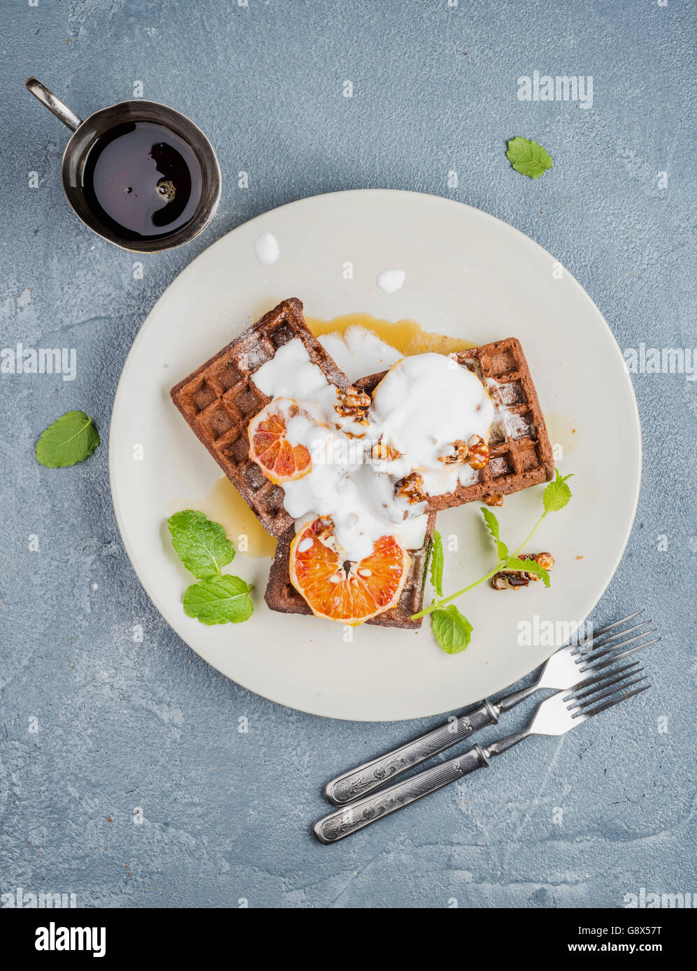 Weiche Waffeln mit Blutorange, Sahne, Marple Sirup und Minze auf weißen Platten über konkrete strukturierten Hintergrund. Ansicht von oben Stockfoto