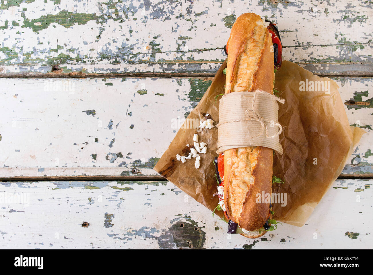 Tapezierte vegetarische Baguette u-Boot-Sandwich mit gegrillter Aubergine, Paprika und Feta Käse auf Backpapier über alte weiße Holz Stockfoto