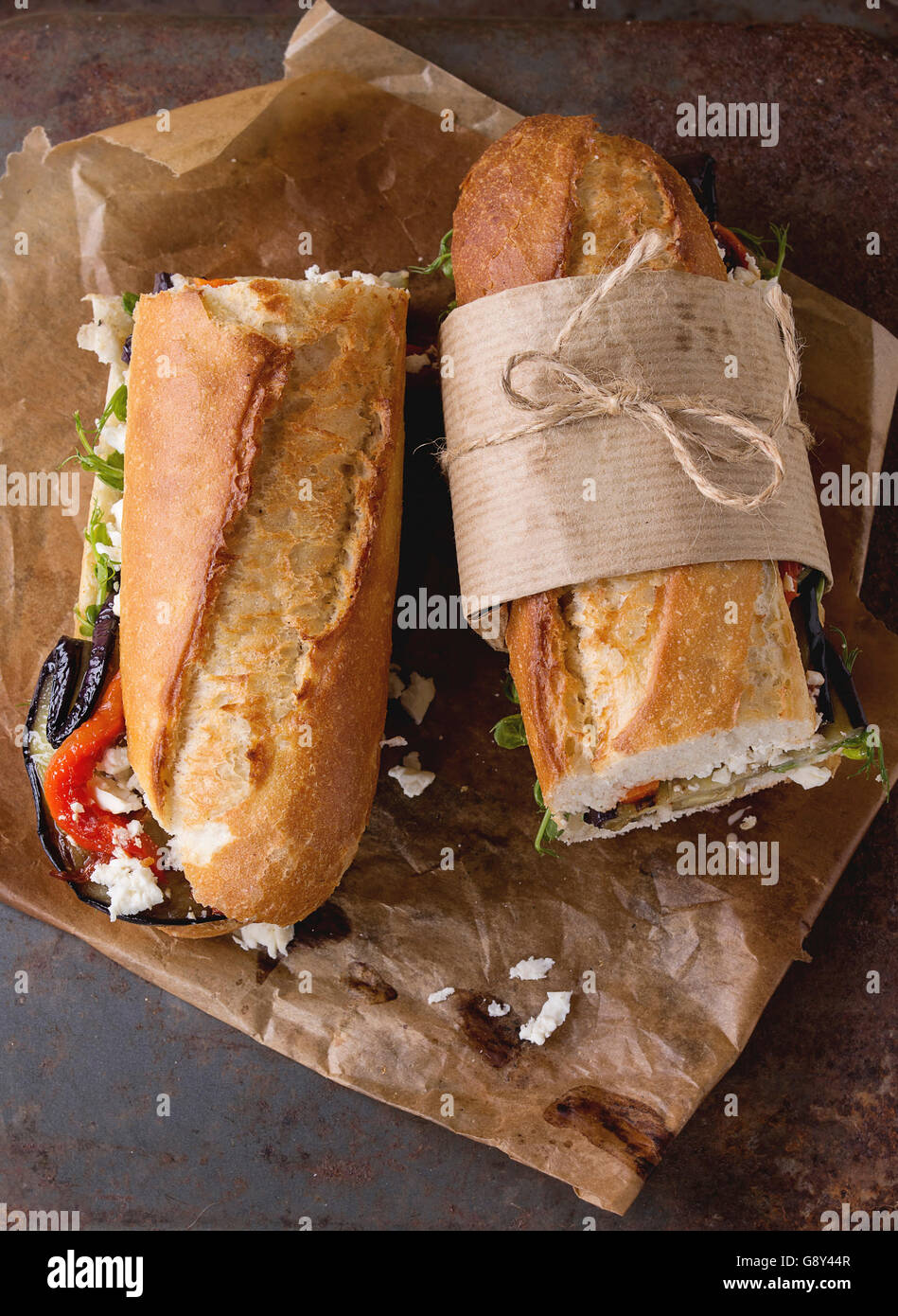 Zwei Hälfte vegetarische Baguette u-Boot-Sandwich mit gegrillter Aubergine, Paprika und Feta Käse auf Backpapier Papier über dunkle Rusty Stockfoto