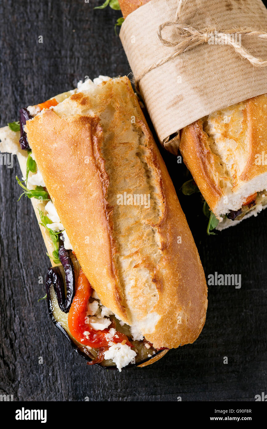 Zwei Hälfte vegetarische Baguette u-Boot-Sandwich mit gegrillter Aubergine, Paprika und Feta Käse auf schwarzem Holz Schneidebrett Stockfoto