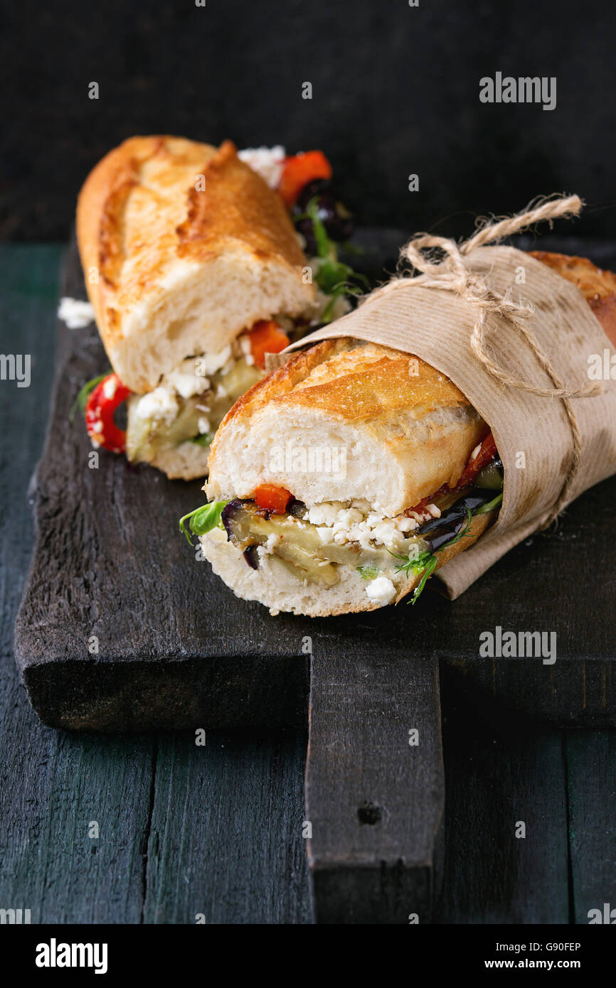 Zwei Hälfte vegetarische Baguette u-Boot-Sandwich mit gegrillter Aubergine, Paprika und Feta Käse auf schwarzem Holz Schneidebrett Stockfoto