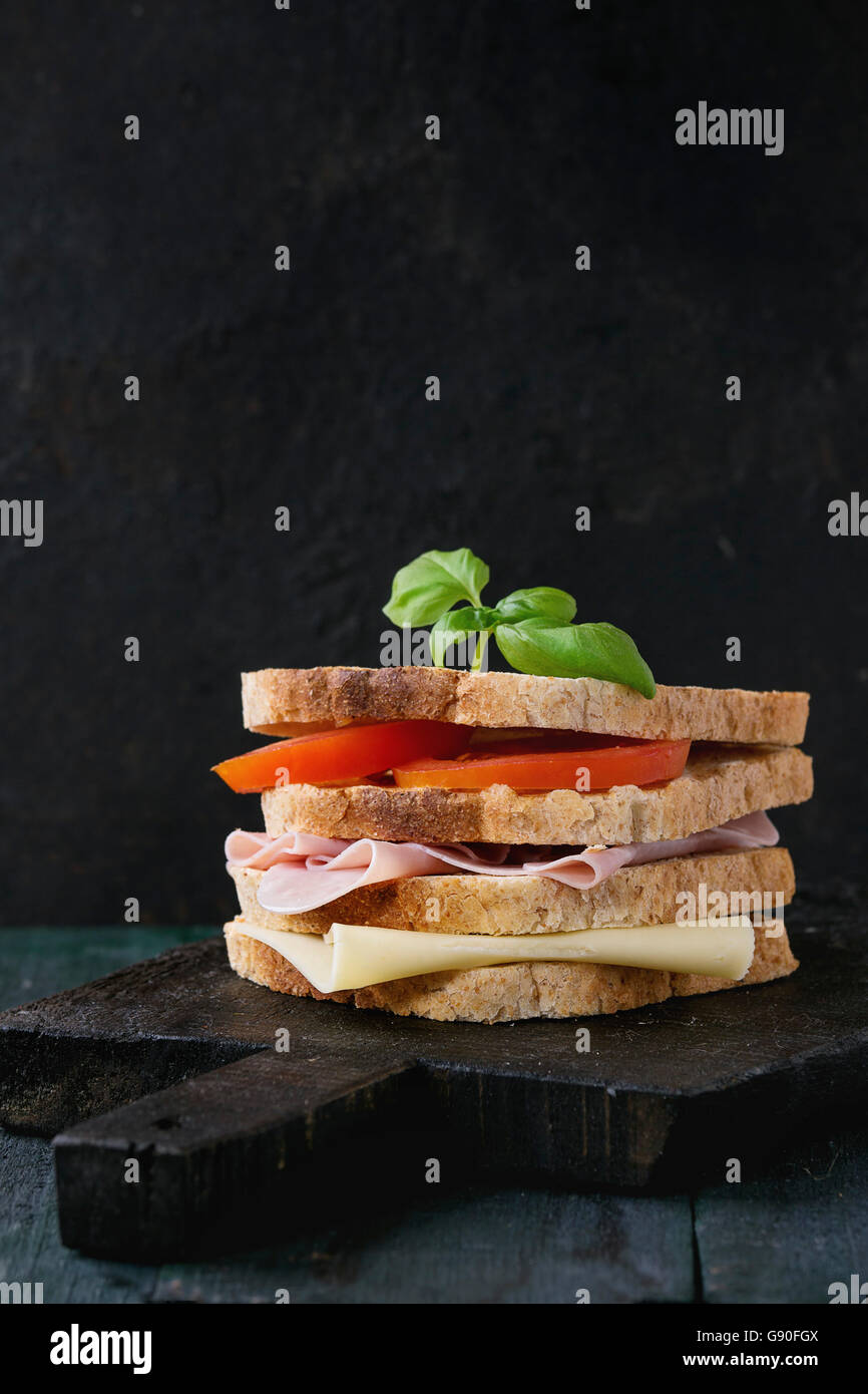 Vollkorn Sandwich-Brot mit Schinken, Käse und Tomaten auf schwarzen Schneidbrett aus Holz über dunklen Hintergrund gegrillt. Stockfoto