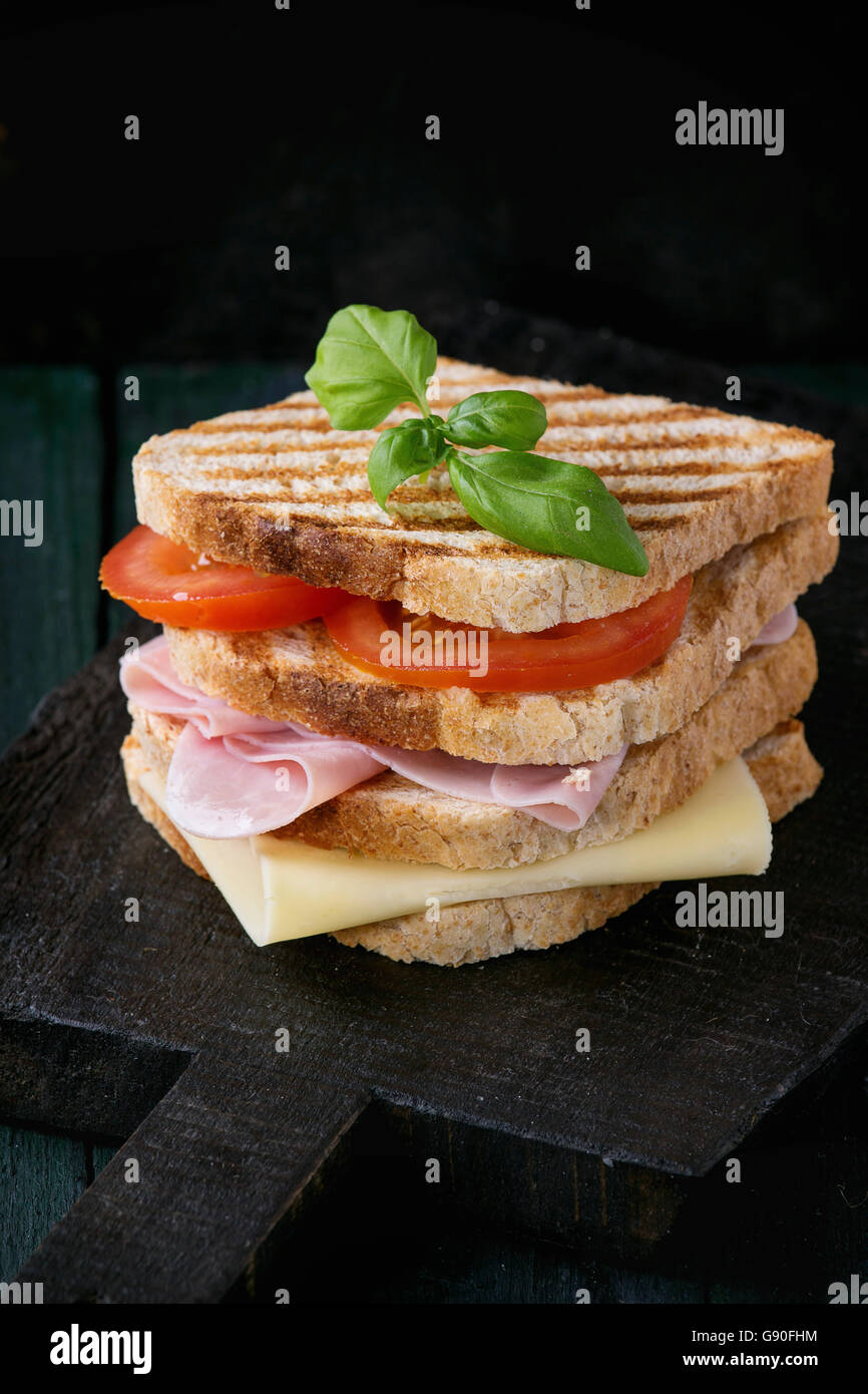 Vollkorn Sandwich-Brot mit Schinken, Käse und Tomaten auf schwarzen Schneidbrett aus Holz über dunklen Hintergrund gegrillt. Stockfoto