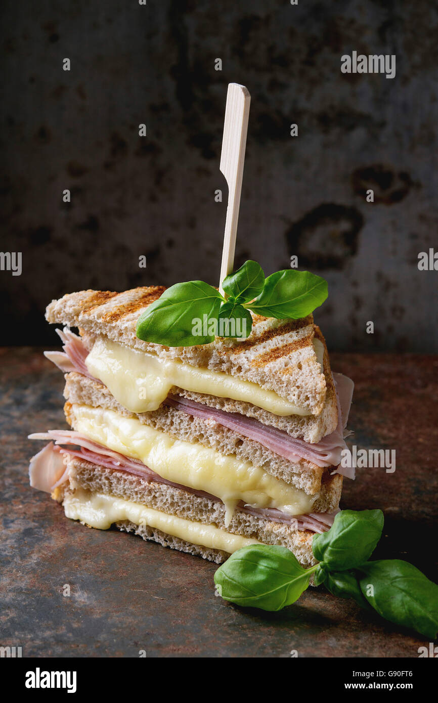 Vollkorn gegrilltes Sandwich-Brot mit schmelzen heiße Käse, Schinken und Basilikum in dunklen rostiges Eisen texturiert Hintergrund. Stockfoto