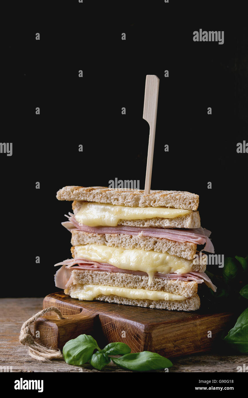 Vollkorn gegrilltes Sandwich-Brot mit schmelzen heiße Käse, Schinken und Basilikum auf Schneidbrett aus Holz in dunklem Hintergrund. Stockfoto