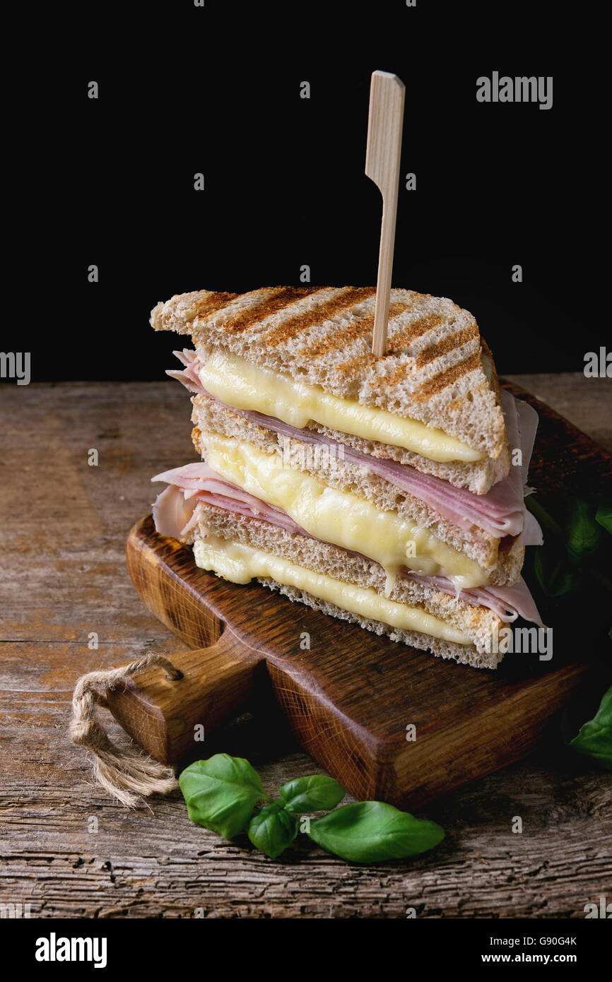 Vollkorn gegrilltes Sandwich-Brot mit schmelzen heiße Käse, Schinken und Basilikum auf Schneidbrett aus Holz in dunklem Hintergrund. Stockfoto