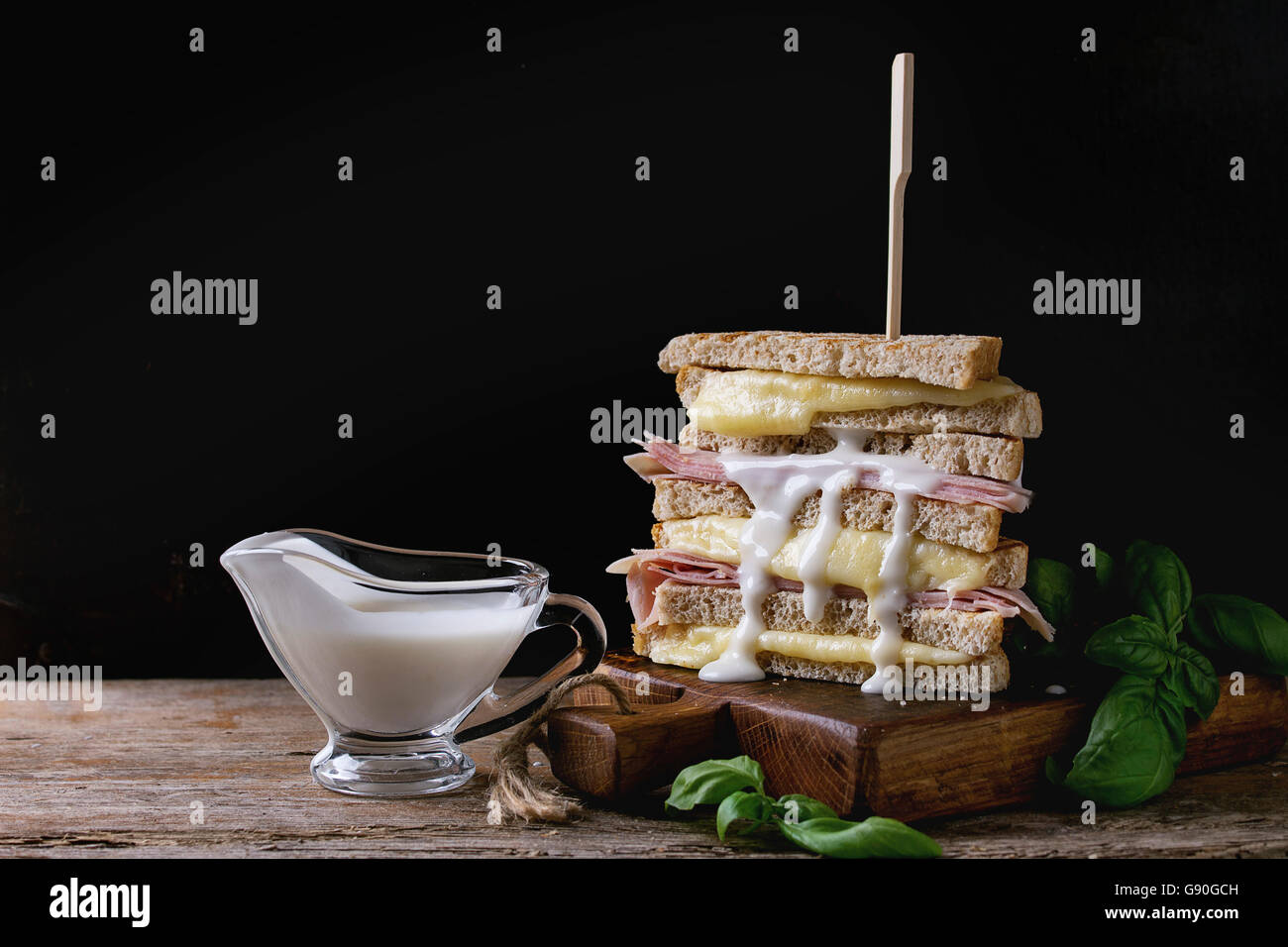 Vollkorn Sandwich-Brot mit schmelzenden heißen Käse, Schinken, Basilikum und gießen Bechamelsauce auf Schneidbrett aus Holz über Dar gegrillt Stockfoto