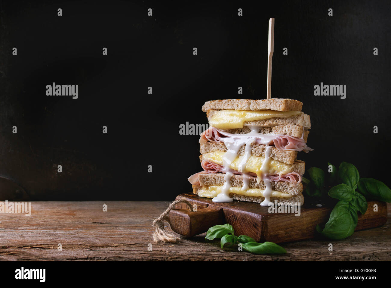Vollkorn Sandwich-Brot mit schmelzenden heißen Käse, Schinken, Basilikum und gießen Bechamelsauce auf Schneidbrett aus Holz über Dar gegrillt Stockfoto