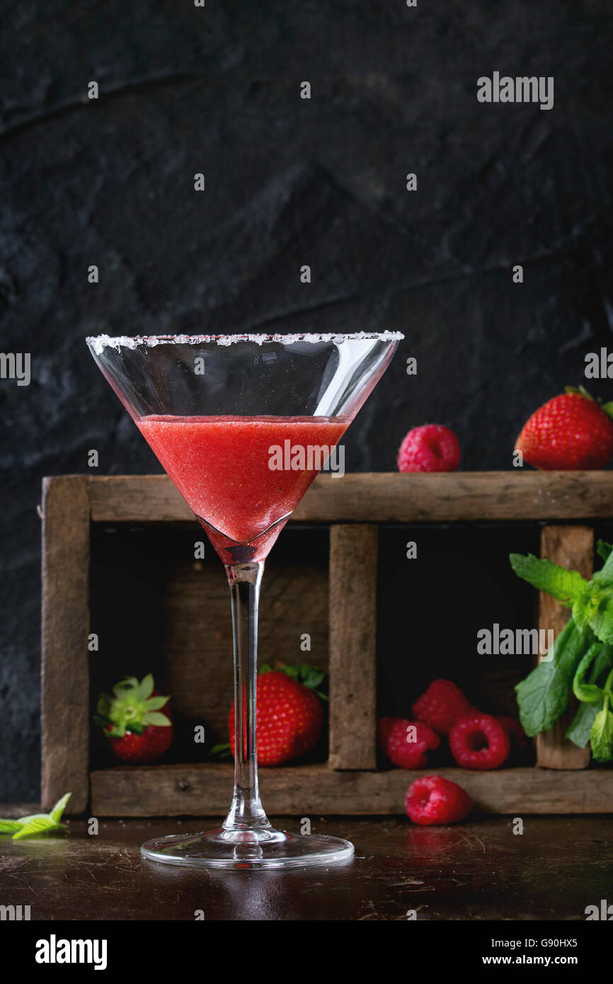 Gezuckerte Glas mit Erdbeer-Dessert-cocktail, serviert auf dunklem Hintergrund mit Erdbeeren, Himbeeren und Minze hinter. Mit c Stockfoto