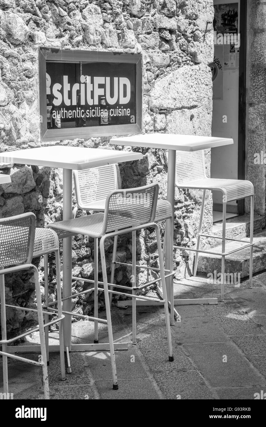 Leere hohe Tische und Stühle auf einem Bürgersteig vor einem Café in Taormina, Sizilien mit dem Zeichen StritFud. Schwarz / weiß Stockfoto