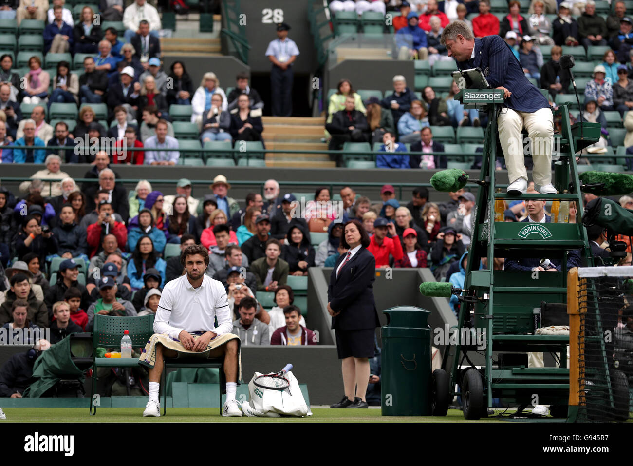 Der Obmann spricht mit Gilles Simon über die Feuchtigkeit auf dem Platz in seinem Match gegen Grigor Dimitrov an Tag drei der Wimbledon Championships bei den All England Lawn Tennis and Croquet Club, Wimbledon. Stockfoto