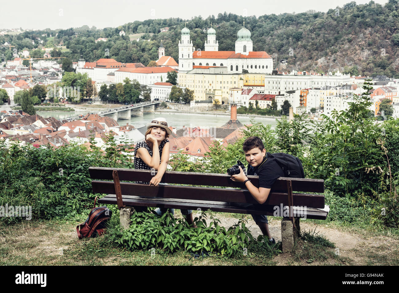 Kaukasische Frau mit Sohn posiert auf der Holzbank mit den Stephansdom in Passau City, Deutschland. Familie unterwegs. Stockfoto