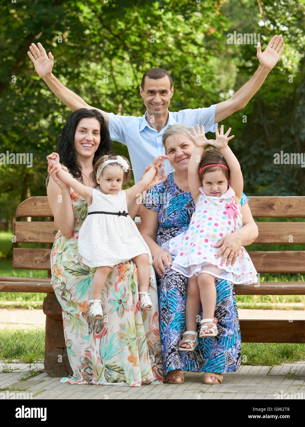 große Familie sitzen auf Holzbank im Stadtpark und winken, Sommer Saison, Kind, Mutter und Großmutter, Gruppe von fünf Personen Stockfoto