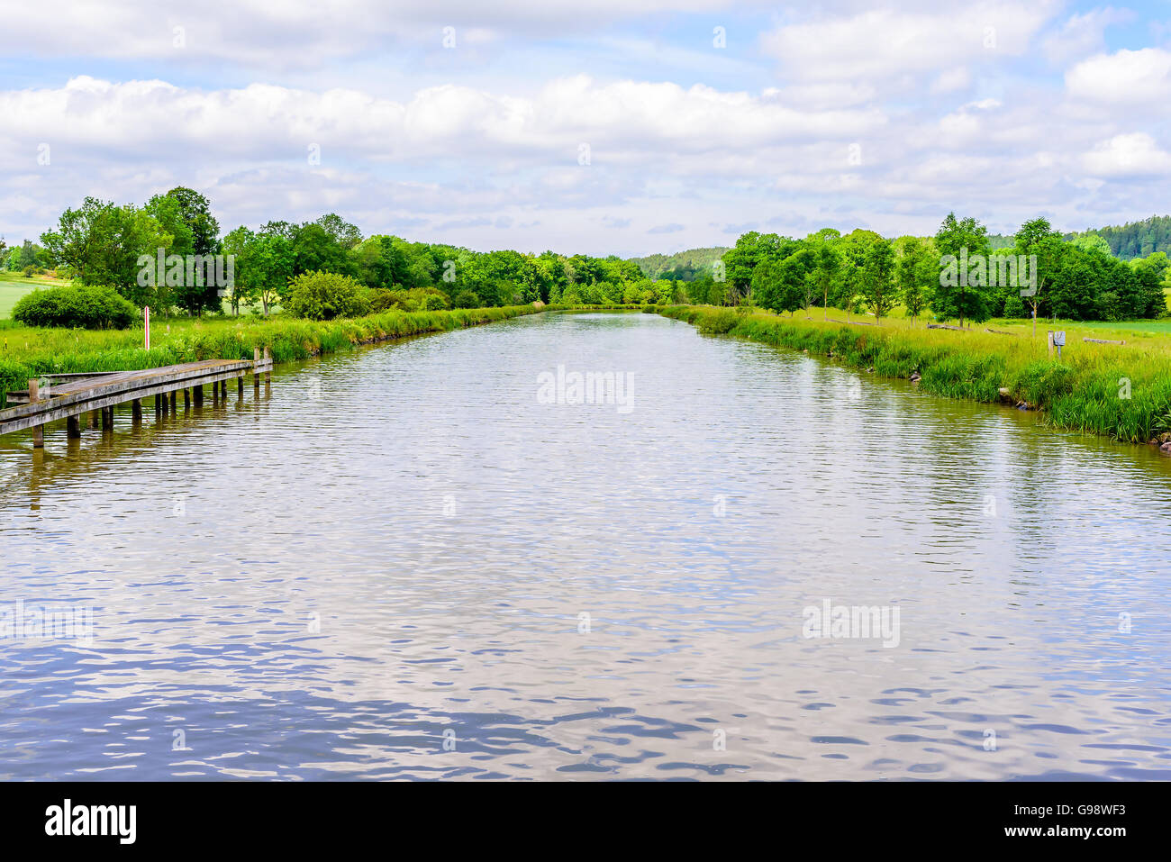 Kleine Strecke des Göta-Kanals mit grünen Bäumen auf beiden Seiten davon. Dies ist in der Nähe des Dorfes Loddby. Einen kleinen Holzsteg ist Stockfoto
