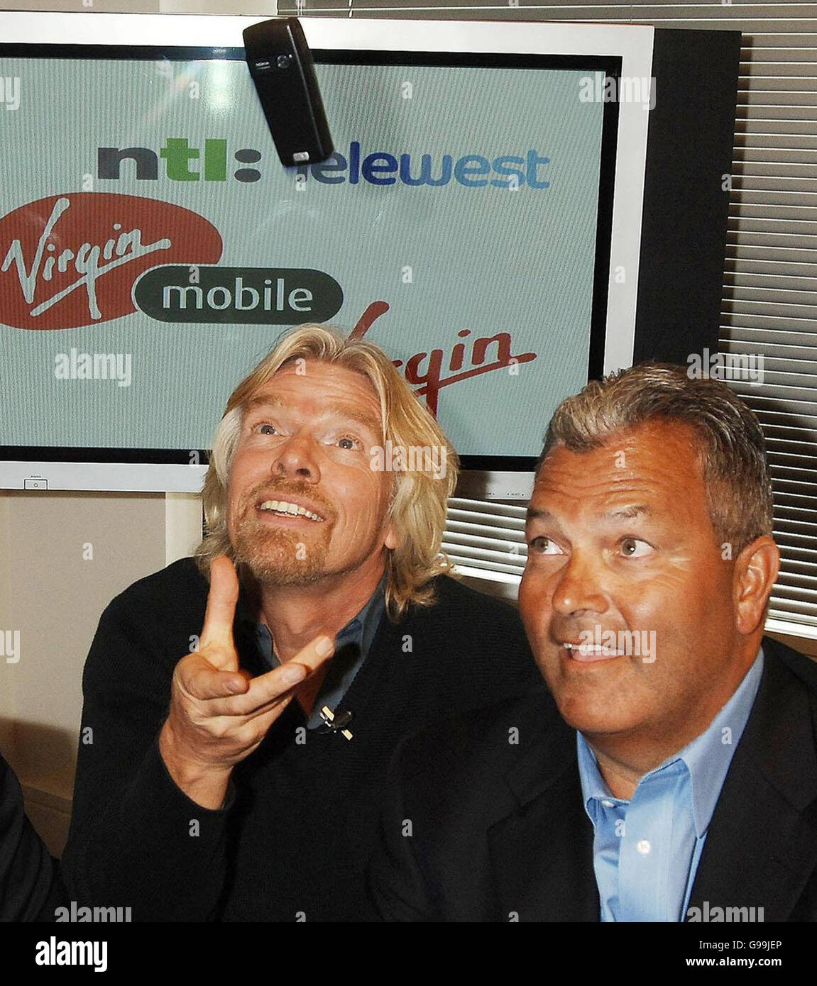 Sir Richard Branson wirft sein Virgin-Handy in die Luft, während er Vorsitzender NTL Telewest Jim Mooney bei einer Pressekonferenz in der Stadt London, Dienstag, den 4. April 2006, sitzt. Nachdem seine Marke Virgin nach der Übernahme seines Virgin Mobile-Geschäfts durch den Kabelgiganten NTL auf 9.4 Millionen britische Haushalte ausgeweitet wurde. Mit der Übernahme von 962.4 Millionen Pfund wird das erste Unternehmen in Großbritannien gegründet, das ein „Quadplay“-Angebot für Kabel-TV, Internetzugang, Festnetztelefonie und Mobilfunkdienste propagiert. Siehe PA Story CITY Virgin. DRÜCKEN Sie VERBANDSFOTO. Bildnachweis sollte lauten: John Stillwell/PA Stockfoto