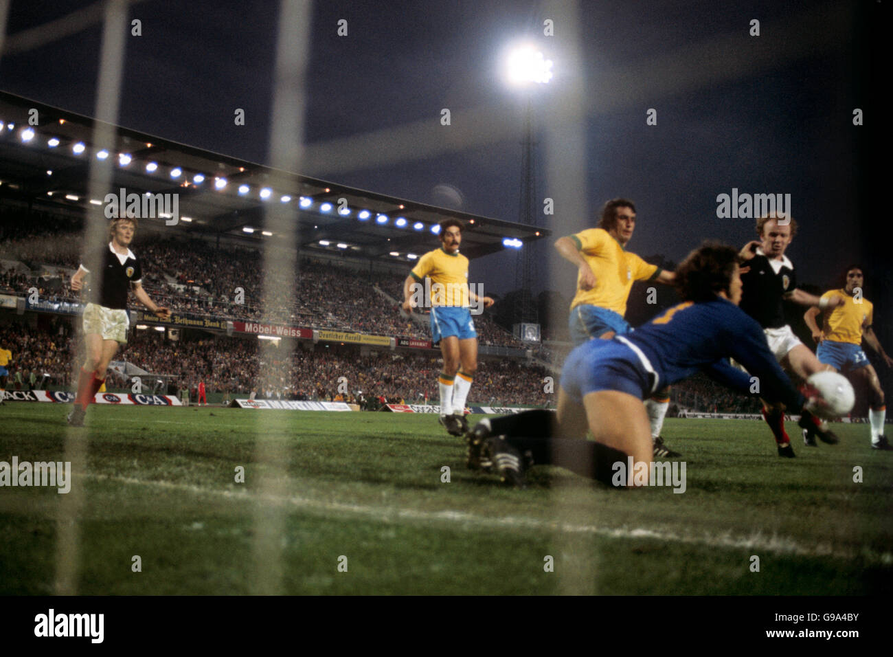 Fußball - Weltmeisterschaft Westdeutschland 1974 - Gruppe 2 - Schottland gegen Brasilien - Waldstadion, Frankfurt. l-r David Hay (Scot) Rivelino, Piazza und Marinho (alle Brasilien) sehen aus, wie Brasiliens Leao zu Füßen von Schottlands Billy Bremner rettet Stockfoto