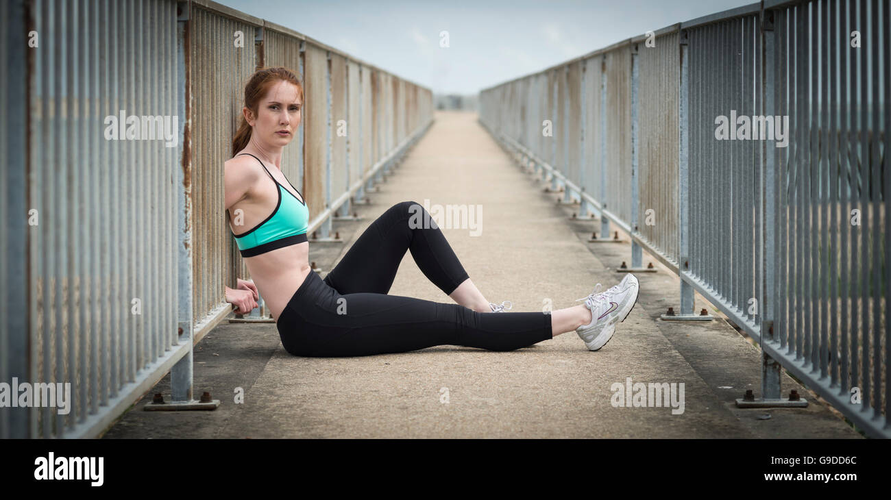 Frau, die Erholung nach dem Training draußen sitzen mit dem Rücken zu Metallgeländer Stockfoto