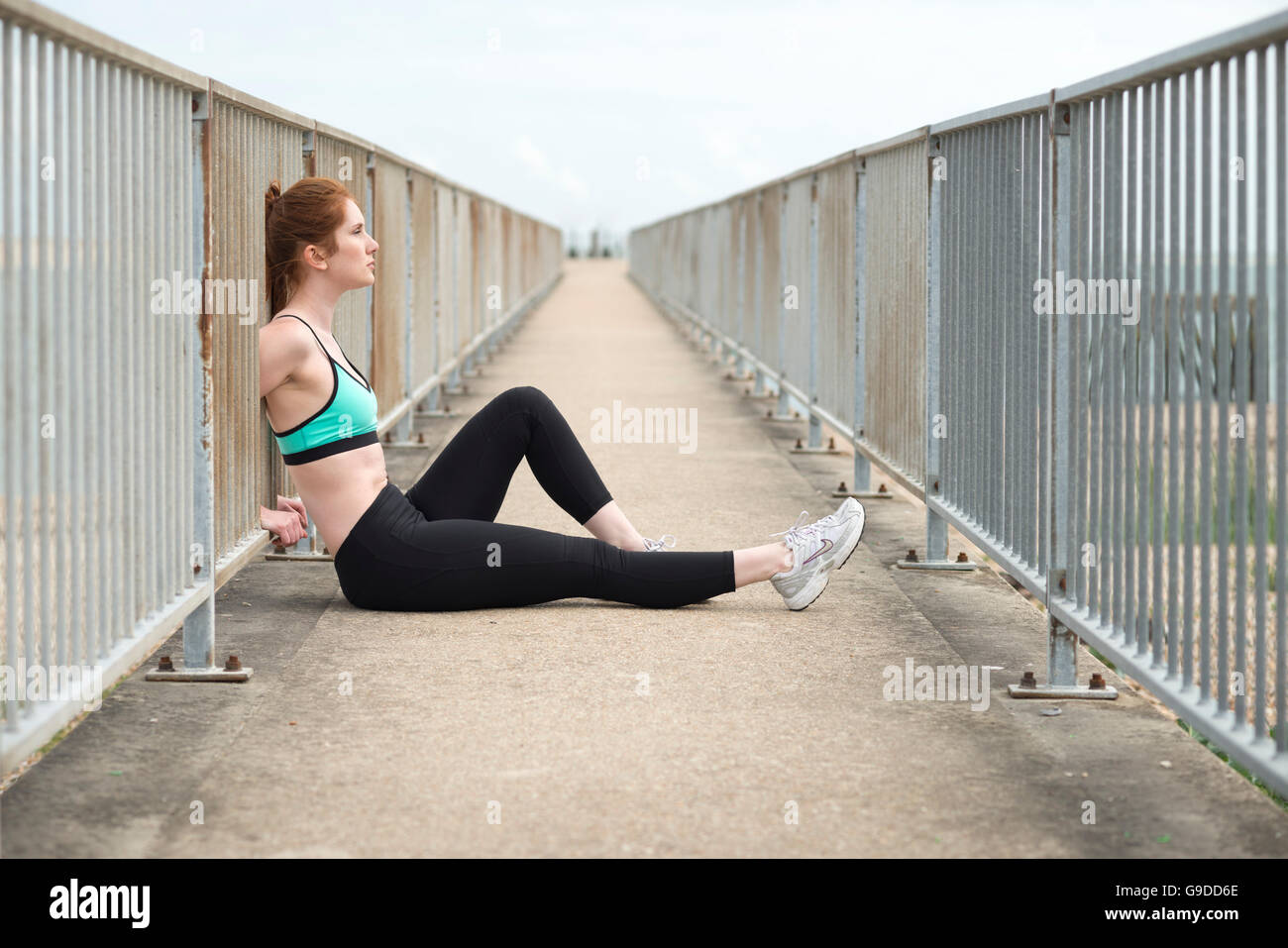 Frau, die Erholung nach dem Training draußen sitzen mit dem Rücken zu Metallgeländer Stockfoto