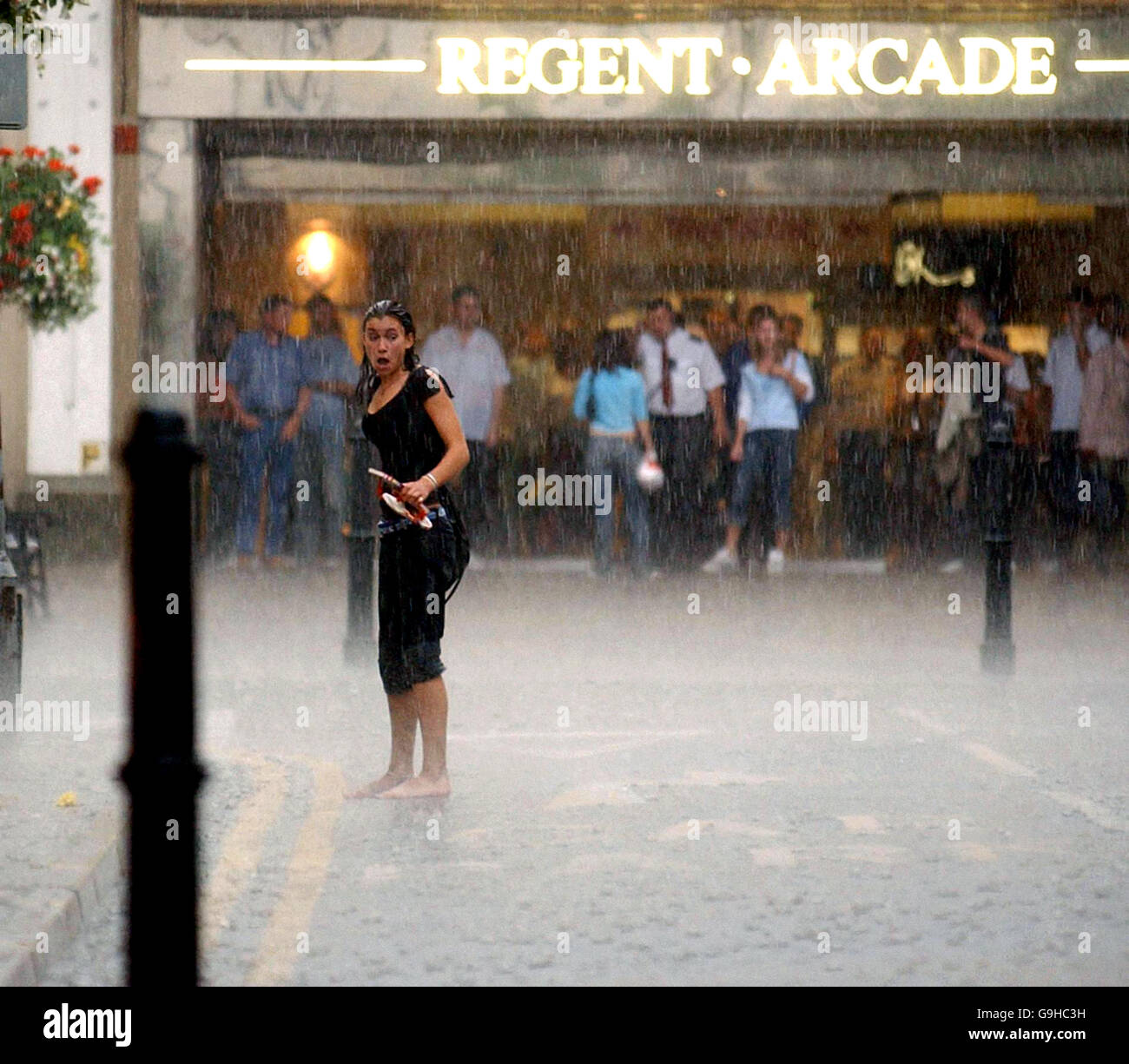 Ein Shopper wird im Regenguss gefangen, während andere im Zentrum von Cheltenham, Gloucestershire, Zuflucht suchen. Stockfoto