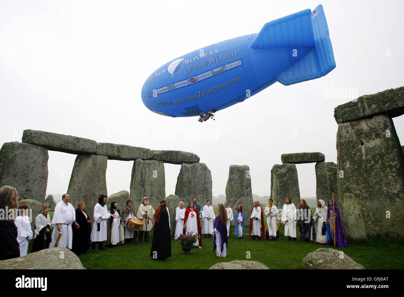 Ein Luftschiff, das die Aufnahme von stonehenge in eine globale Shortlist der sieben Wunder der modernen Welt verkündet, fliegt über den Himmel, während Druiden eine Samhain- oder heidnische Halloween-Segenszeremonie in Stonehenge in Wiltshire durchführen. Stockfoto