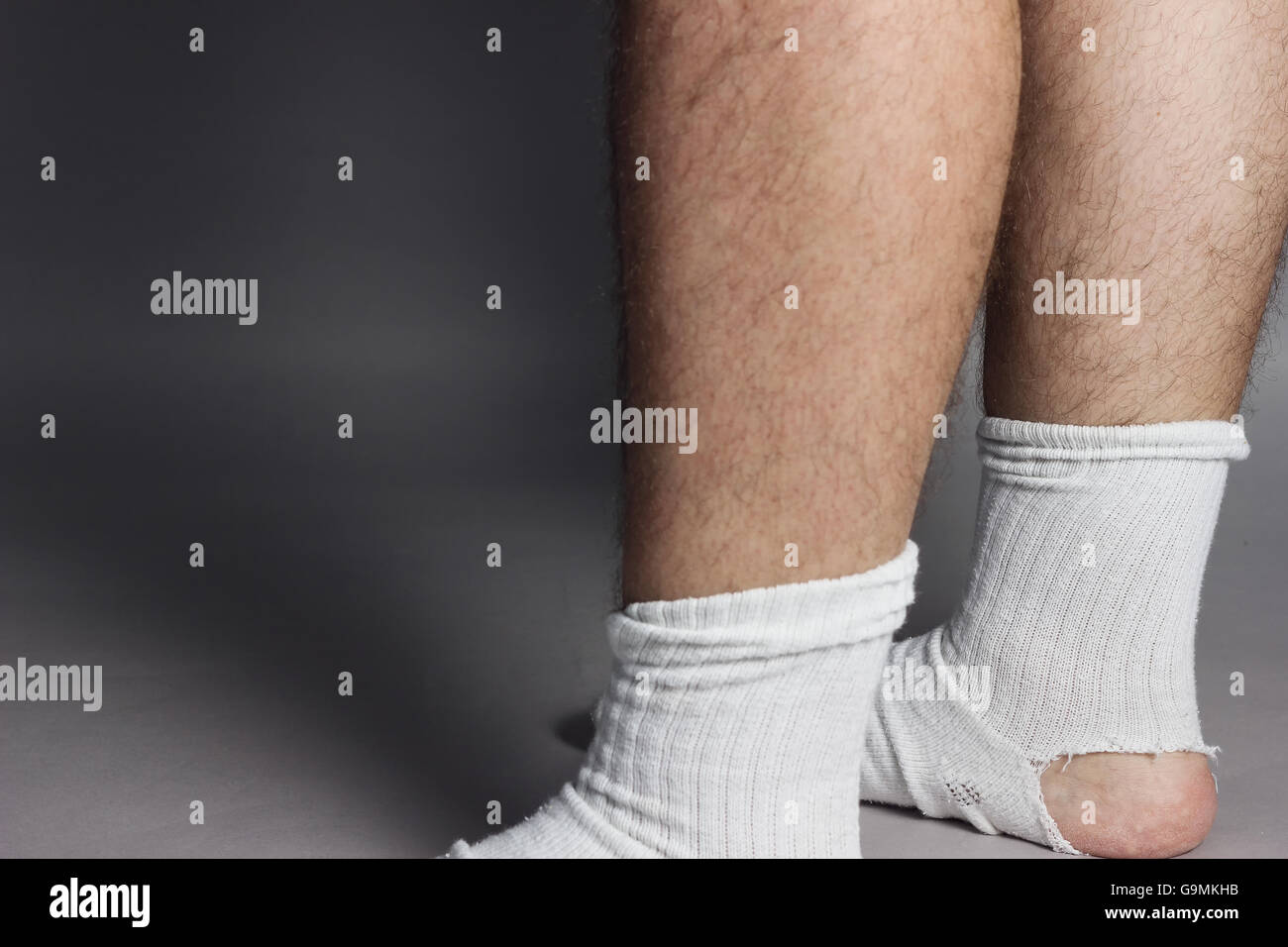 stehende Füße mit weißen Socken und ein großes Loch vor grauem Hintergrund Stockfoto