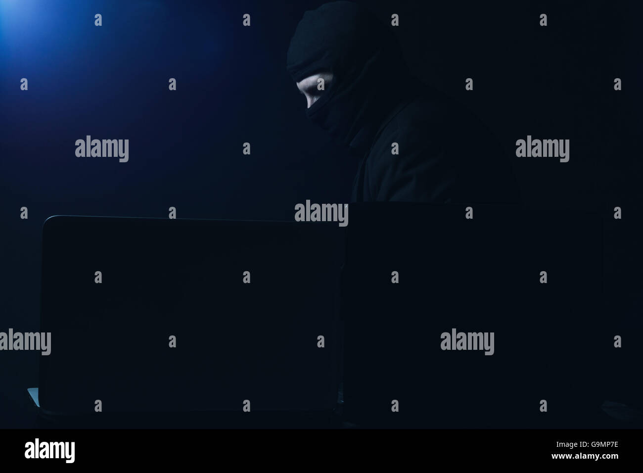 Computer-Hacker im Anzug stehlen Daten von Laptop vor schwarzem Hintergrund und blauem Licht Stockfoto