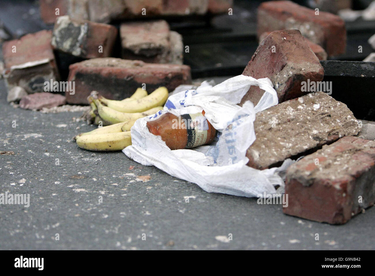 Der Inhalt einer Einkaufstasche liegt zwischen Ziegeln aus einer gefallenen Mauer auf Fern Close, Stockport. Stockfoto