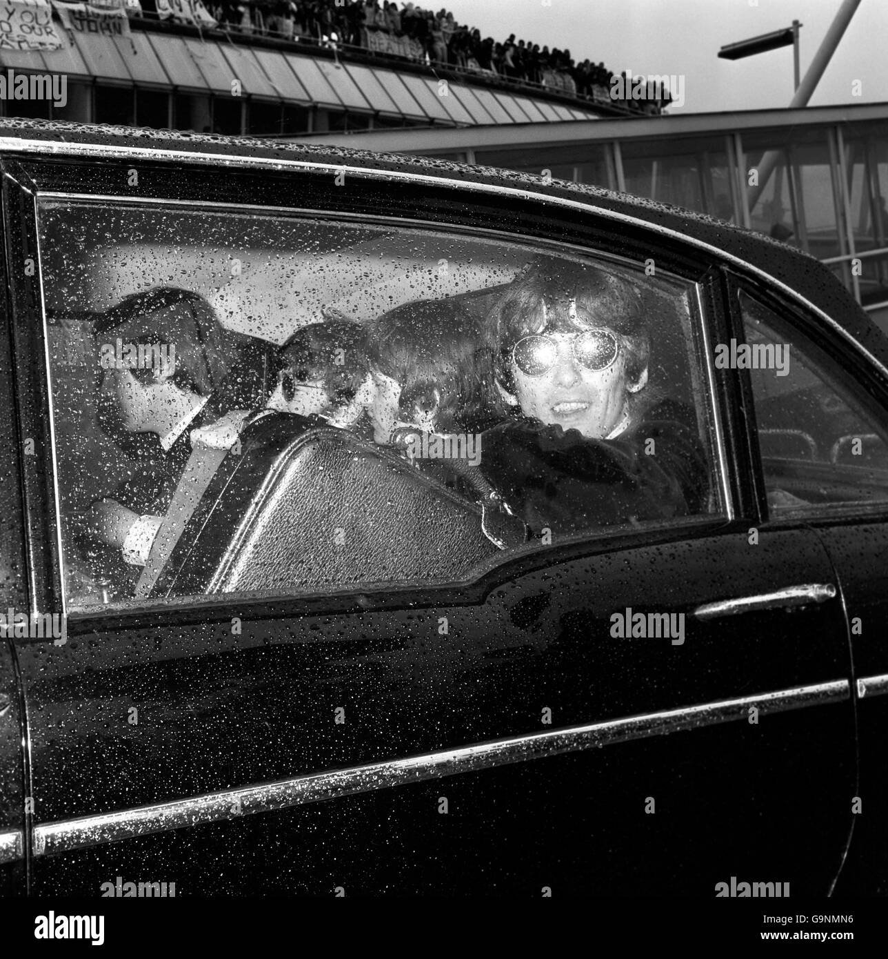 Mit dem Gepäck in ein kleines Auto gepfercht, gehen die Beatles am Flughafen London zum Flugzeug, als sie zu einer Tour in die Vereinigten Staaten von Amerika aufmachten. Durch das regengesprenkelte Fenster gesehen sind: Paul McCartney, John Lennon, Ringo Starr und George Harrison. Stockfoto