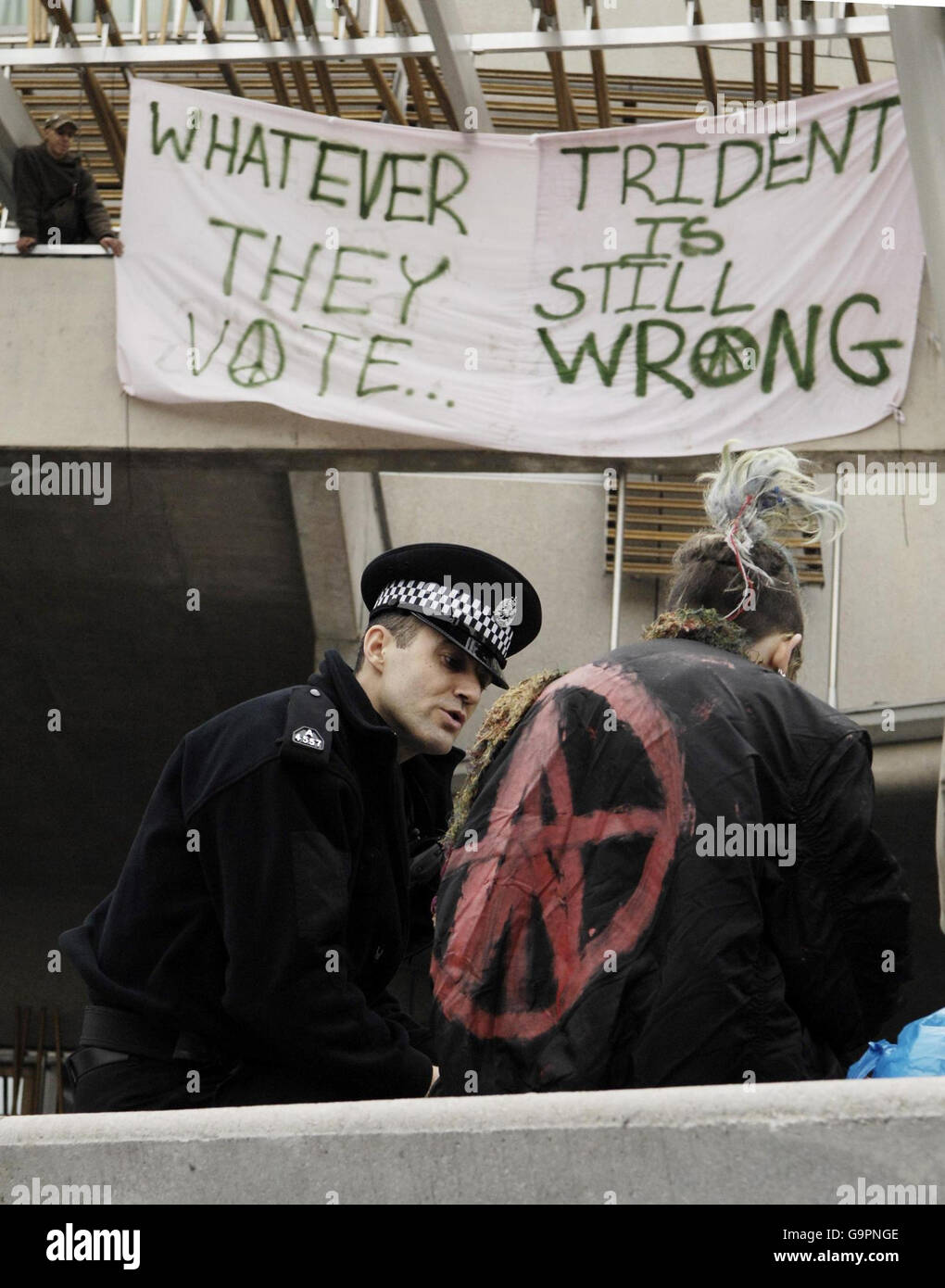 Ein Polizeibeamter spricht mit einem Anti-Trident-Protestler, während ein anderer Protestler ein Banner auf dem schottischen Parlament in Edinburgh auflegt. Stockfoto