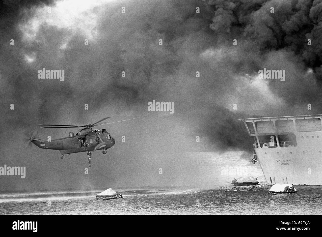Während des verheerenden Luftangriffs auf Sir Galahad und Sir Tristram schwebt ein Hubschrauber des Royal Navy Sea King über Rettungsflößen, um Überlebende des brennenden britischen Landungsschiffs RFA Sir Galahad abzuholen. Stockfoto